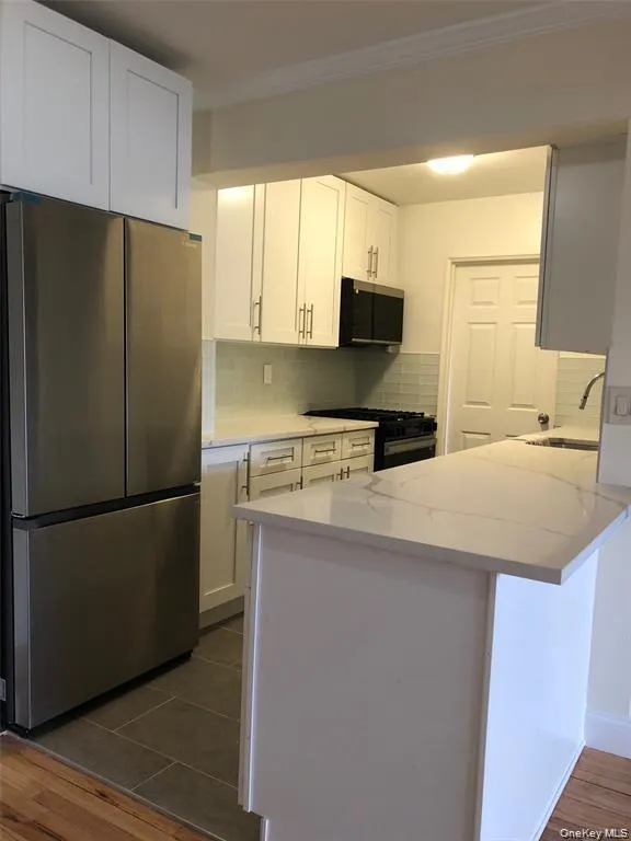 Kitchen with appliances with stainless steel finishes, white cabinets, tasteful backsplash, dark wood-style floors, and a peninsula Kitchen with appliances with stainless steel finishes, white cabinets, tasteful backsplash, dark wood-style floors, and a peninsula