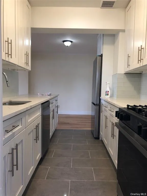 Kitchen with stainless steel appliances, backsplash, white cabinetry, and dark tile patterned flooring Kitchen with stainless steel appliances, backsplash, white cabinetry, and dark tile patterned flooring