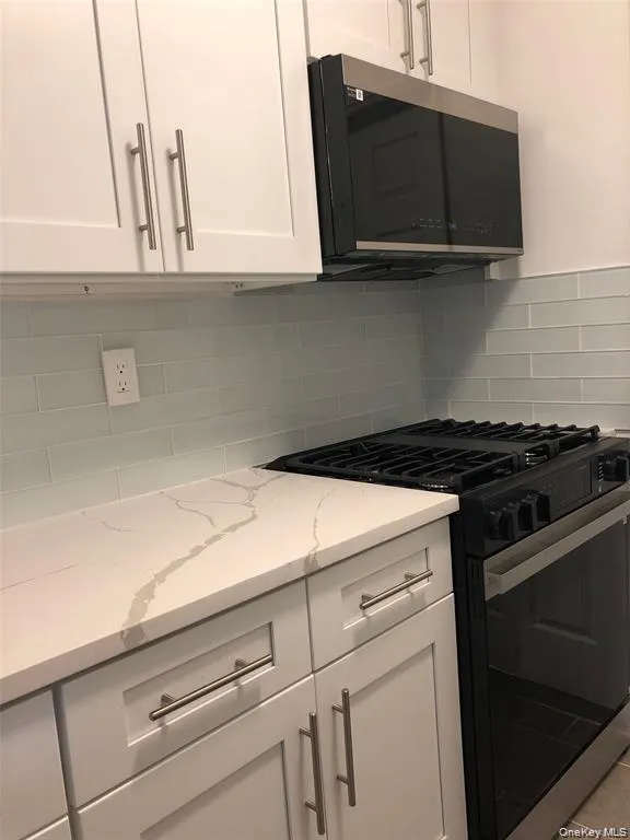 Kitchen with gas range, white cabinetry, stainless steel microwave, and light stone countertops Kitchen with gas range, white cabinetry, stainless steel microwave, and light stone countertops
