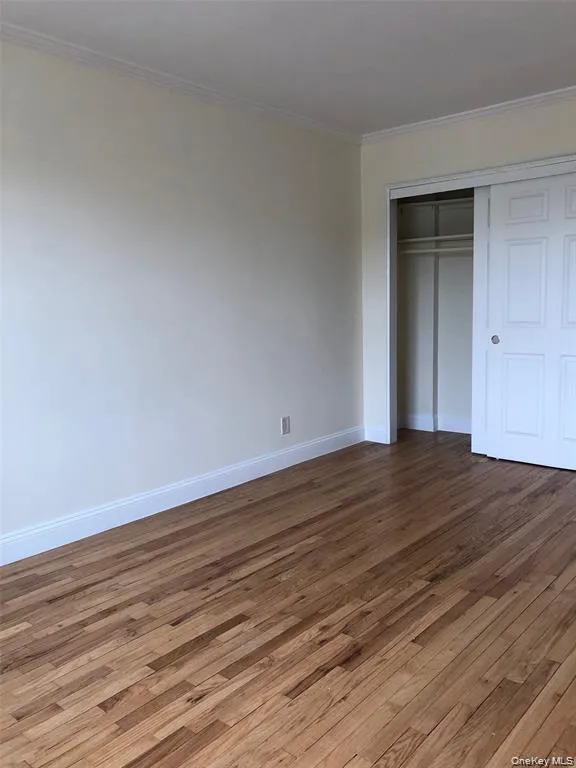 Unfurnished bedroom featuring dark wood-type flooring, a closet, and crown molding Unfurnished bedroom featuring dark wood-type flooring, a closet, and crown molding