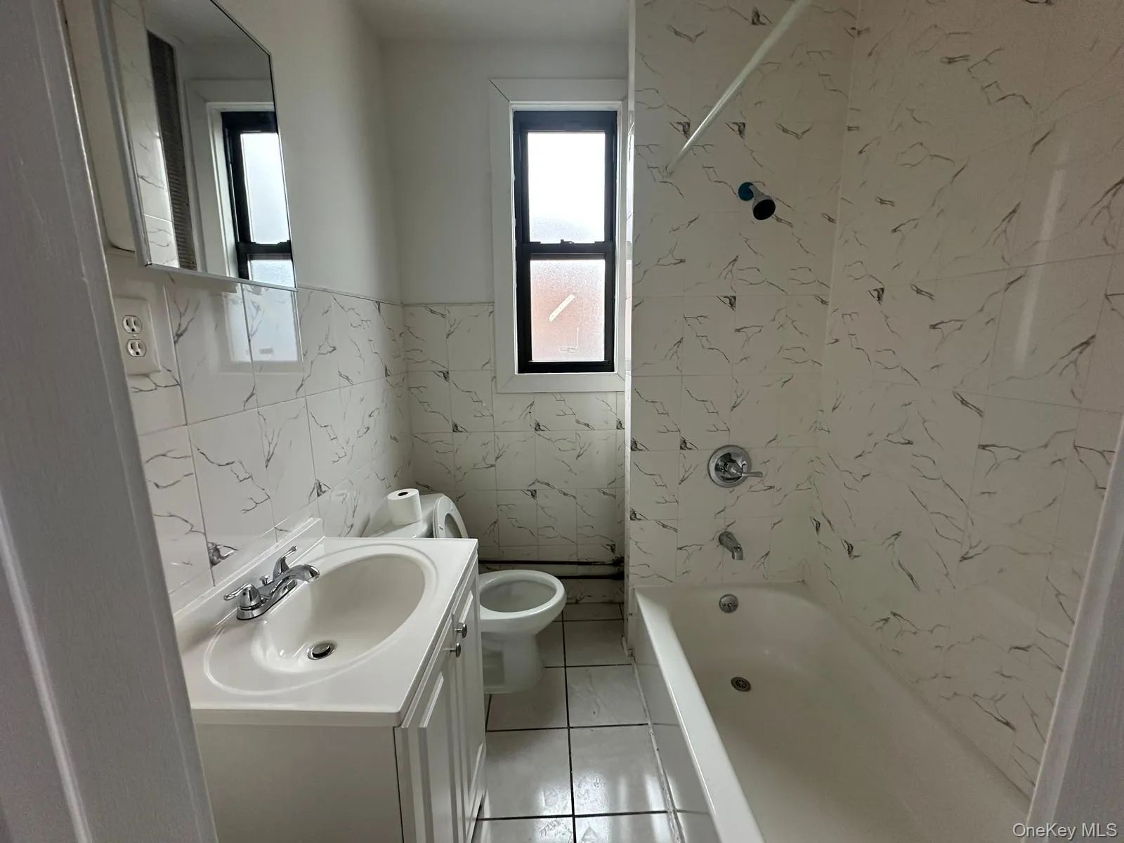 Bathroom with tile walls, vanity, shower / washtub combination, wainscoting, and light tile patterned floors Bathroom with tile walls, vanity, shower / washtub combination, wainscoting, and light tile patterned floors