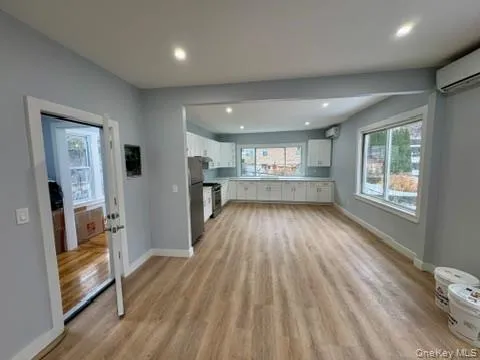 Unfurnished living room featuring light wood-style flooring, a wall unit AC, and recessed lighting Unfurnished living room featuring light wood-style flooring, a wall unit AC, and recessed lighting