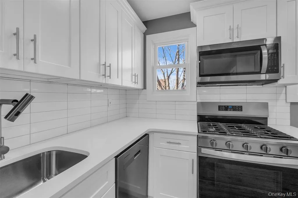 Kitchen with appliances with stainless steel finishes, white cabinetry, backsplash, and light stone countertops Kitchen with appliances with stainless steel finishes, white cabinetry, backsplash, and light stone countertops