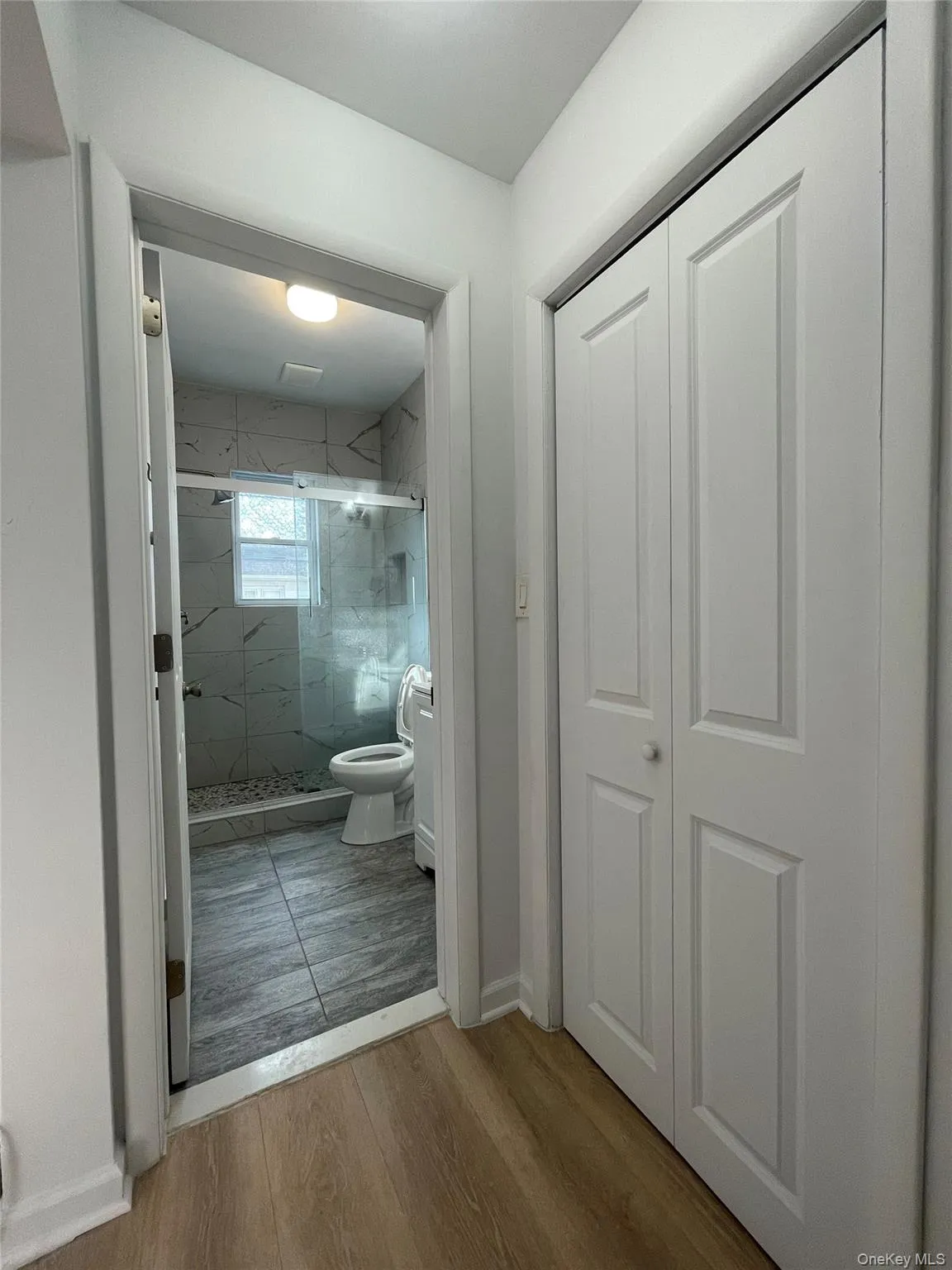 Full bathroom with a marble finish shower and light wood-style floors Full bathroom with a marble finish shower and light wood-style floors