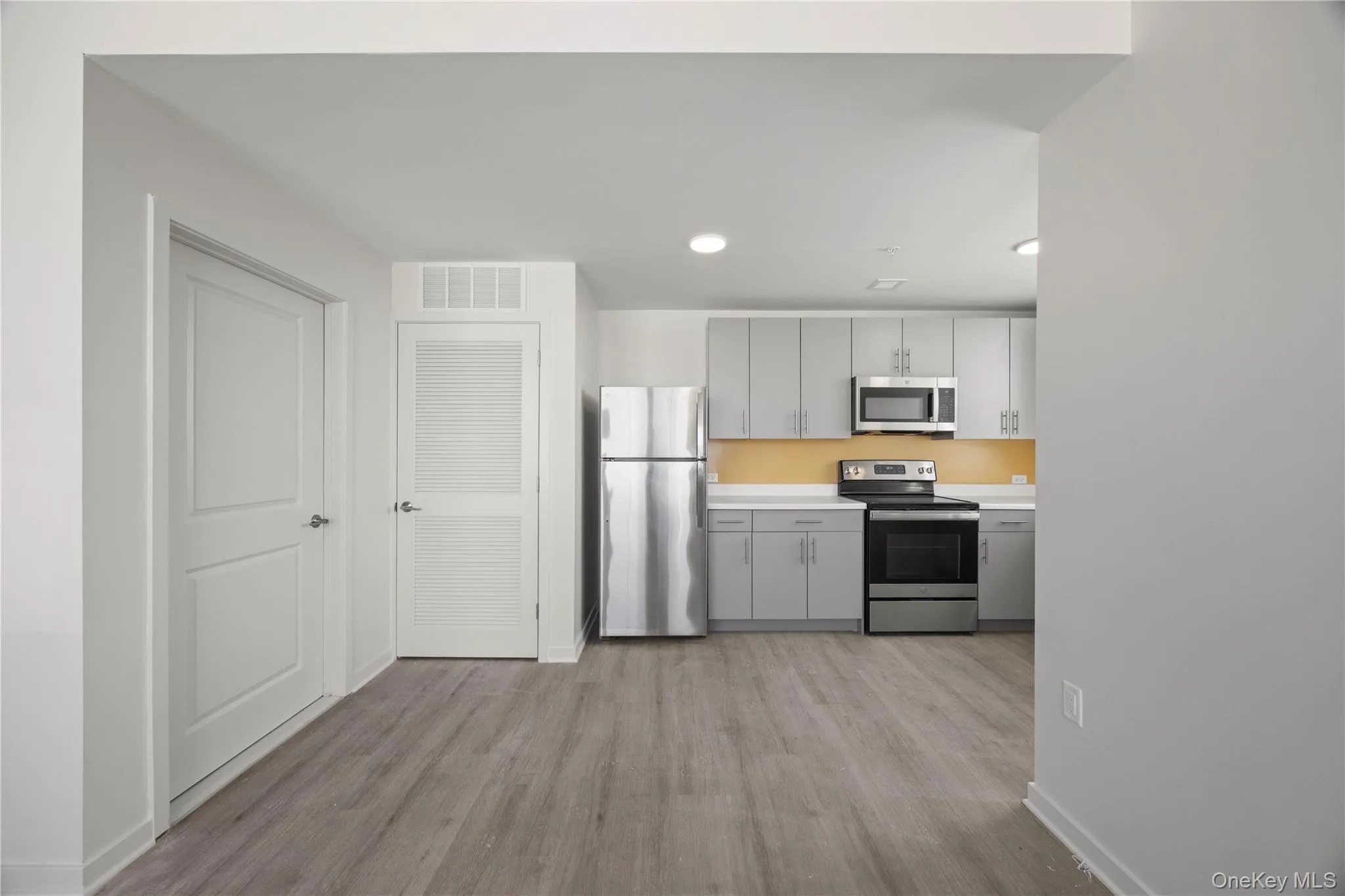 Kitchen with light countertops, stainless steel appliances, gray cabinets, light wood-type flooring, and recessed lighting Kitchen with light countertops, stainless steel appliances, gray cabinets, light wood-type flooring, and recessed lighting
