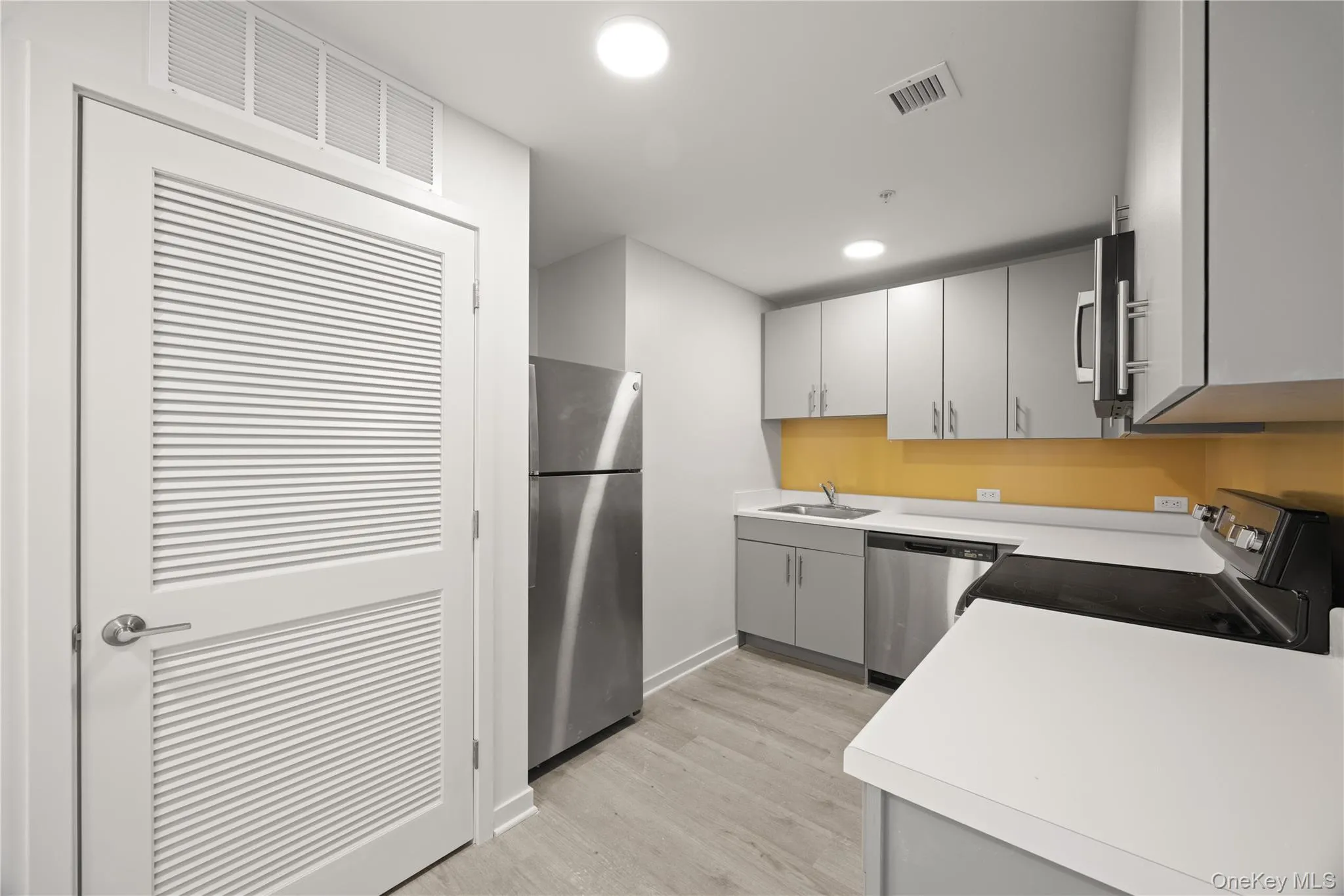 Kitchen featuring light countertops, appliances with stainless steel finishes, gray cabinets, light wood finished floors, and recessed lighting Kitchen featuring light countertops, appliances with stainless steel finishes, gray cabinets, light wood finished floors, and recessed lighting