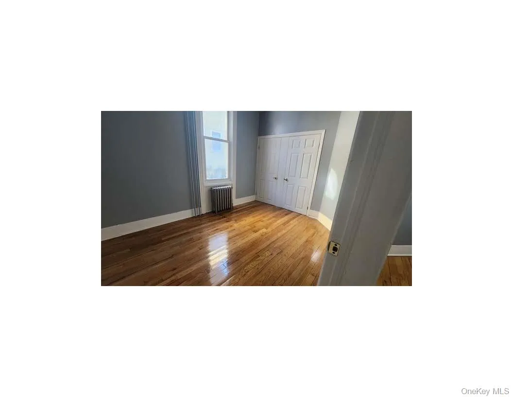 Unfurnished bedroom with radiator, light wood finished floors, and a closet Unfurnished bedroom with radiator, light wood finished floors, and a closet