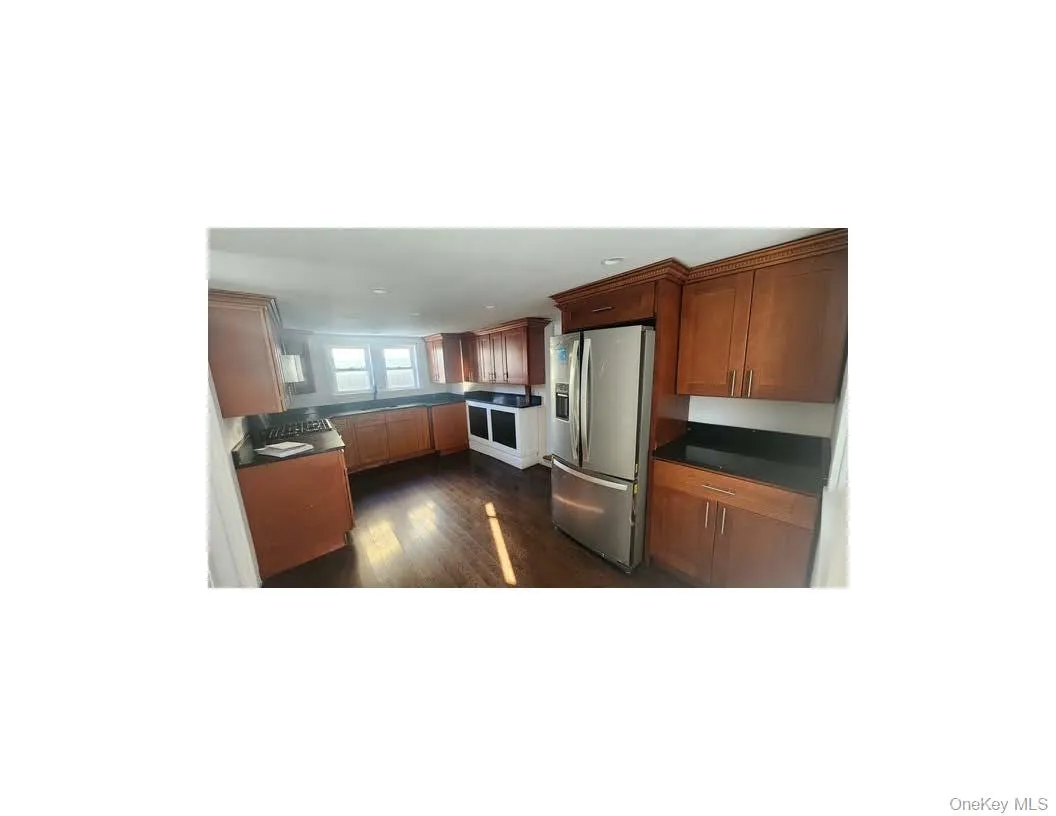 Kitchen with dark countertops, stainless steel refrigerator with ice dispenser, dark wood-type flooring, and brown cabinetry Kitchen with dark countertops, stainless steel refrigerator with ice dispenser, dark wood-type flooring, and brown cabinetry