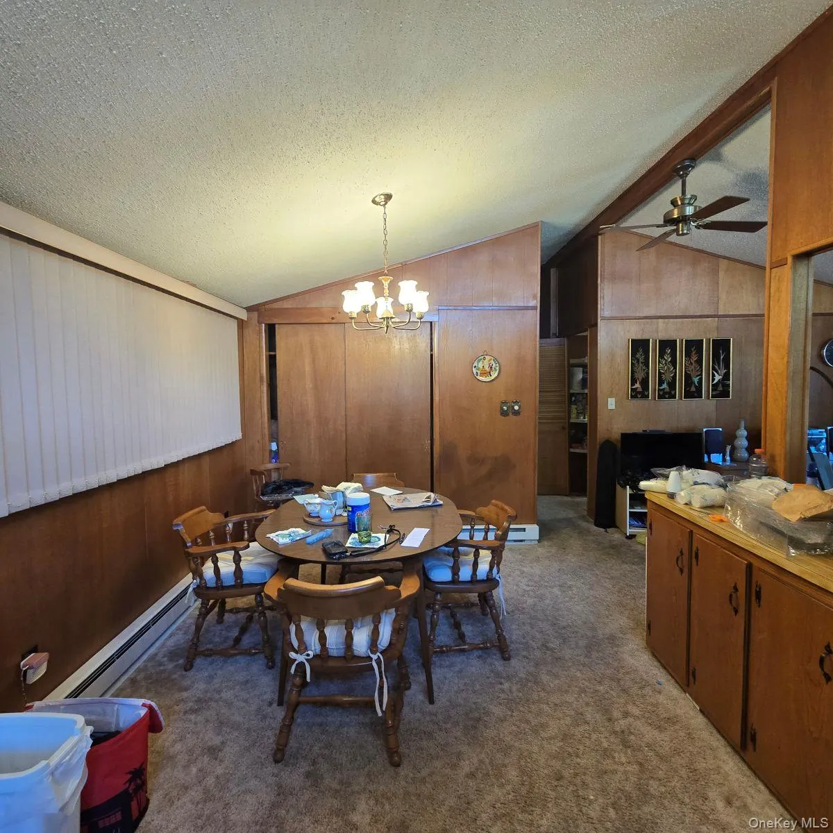 Carpeted dining area featuring a textured ceiling, lofted ceiling, a ceiling fan, a chandelier, and wood walls Carpeted dining area featuring a textured ceiling, lofted ceiling, a ceiling fan, a chandelier, and wood walls