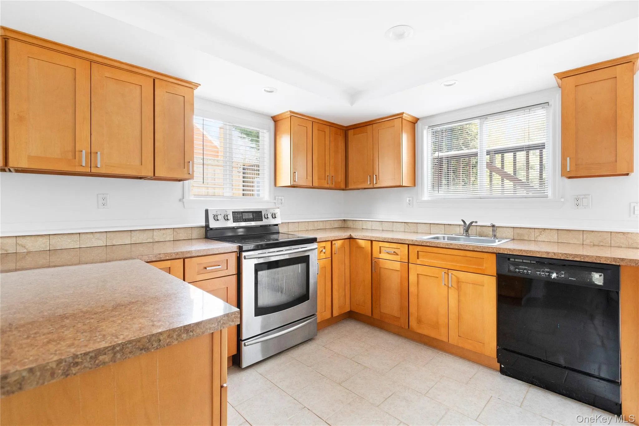 Kitchen featuring stainless steel electric range, black dishwasher, brown cabinetry, recessed lighting, and light countertops Kitchen featuring stainless steel electric range, black dishwasher, brown cabinetry, recessed lighting, and light countertops