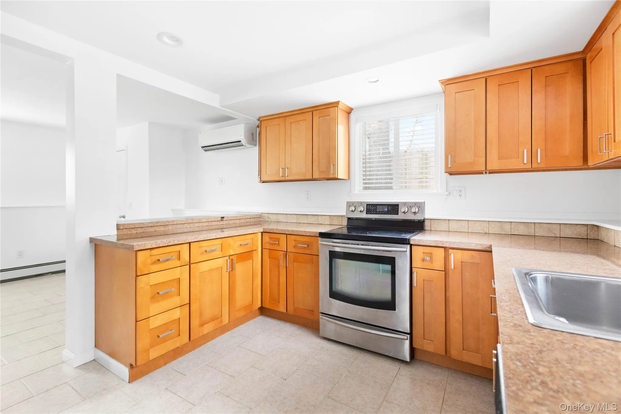 Kitchen featuring stainless steel electric stove, light countertops, a peninsula, a wall unit AC, and recessed lighting Kitchen featuring stainless steel electric stove, light countertops, a peninsula, a wall unit AC, and recessed lighting