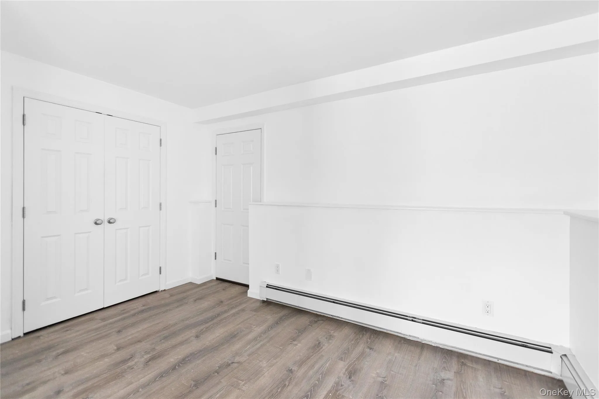 Unfurnished bedroom with a baseboard heating unit, wood finished floors, and a closet Unfurnished bedroom with a baseboard heating unit, wood finished floors, and a closet