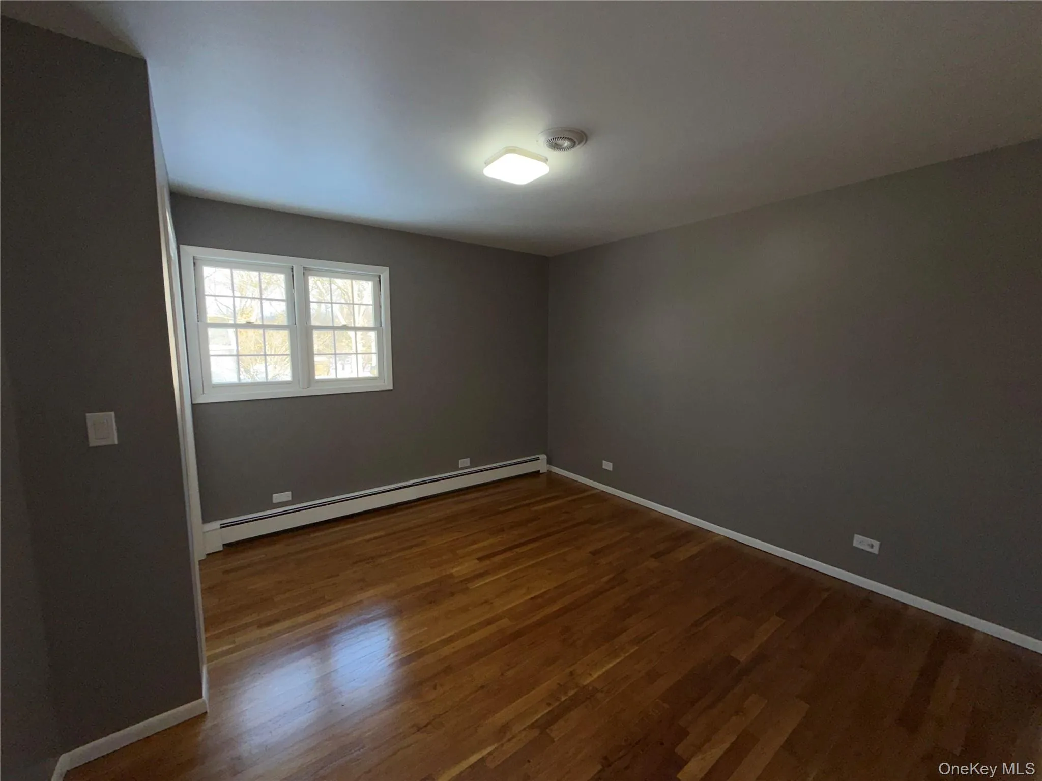 Spare room featuring baseboard heating and dark wood finished floors Spare room featuring baseboard heating and dark wood finished floors