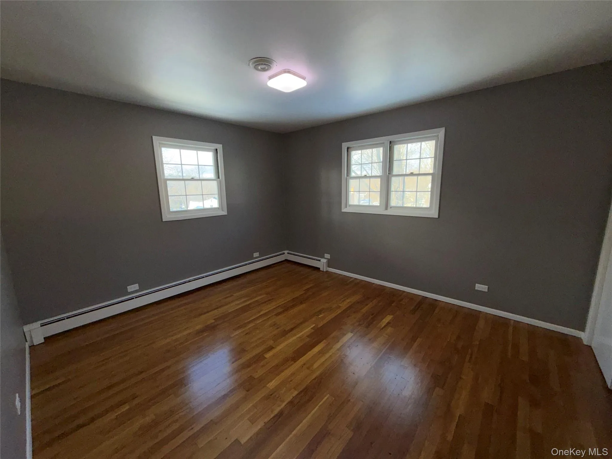 Empty room with dark wood-style flooring, a baseboard radiator, and plenty of natural light Empty room with dark wood-style flooring, a baseboard radiator, and plenty of natural light