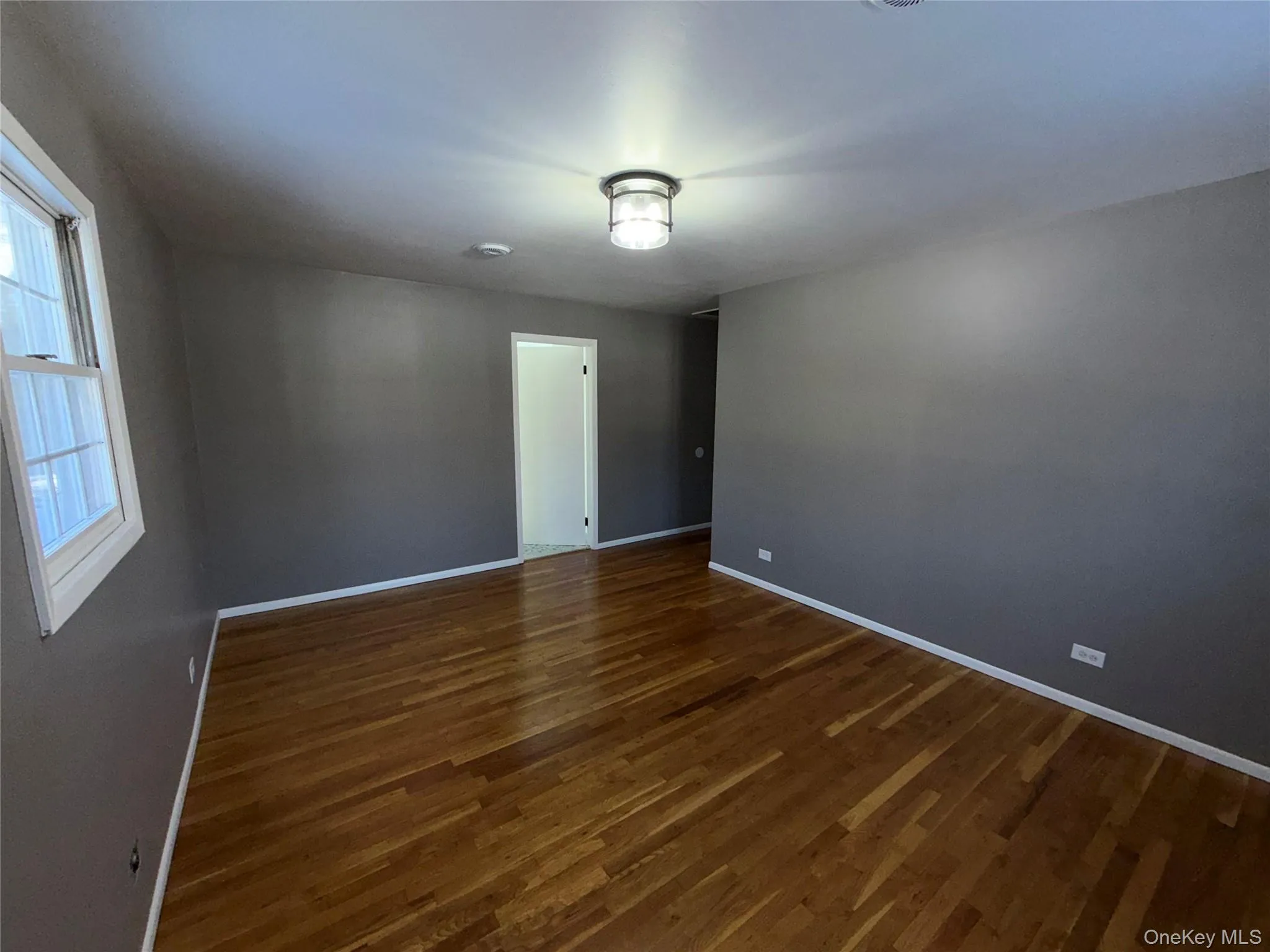 Empty room with dark wood-type flooring and baseboards Empty room with dark wood-type flooring and baseboards