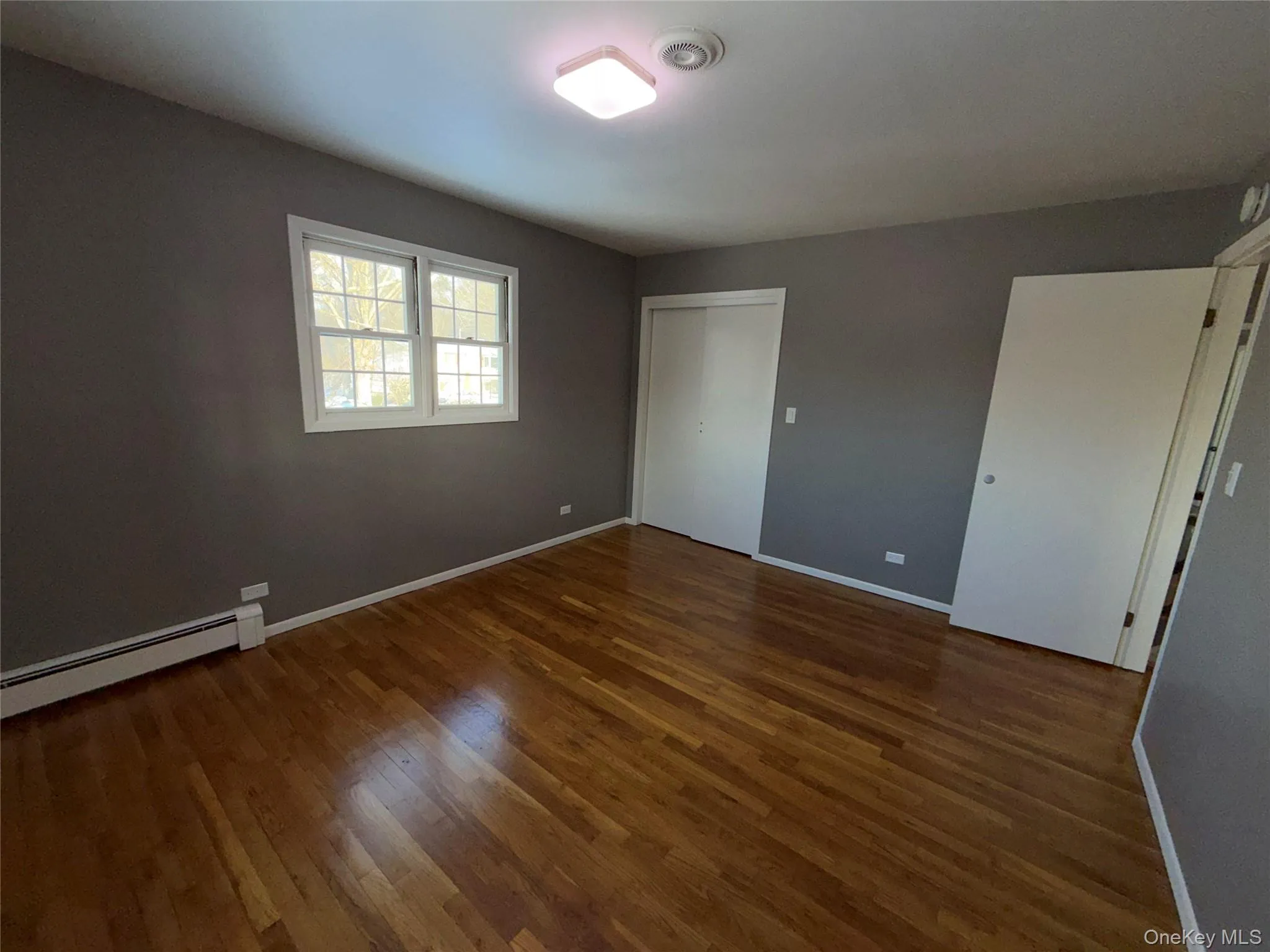 Unfurnished bedroom with a baseboard heating unit, dark wood-type flooring, and a closet Unfurnished bedroom with a baseboard heating unit, dark wood-type flooring, and a closet