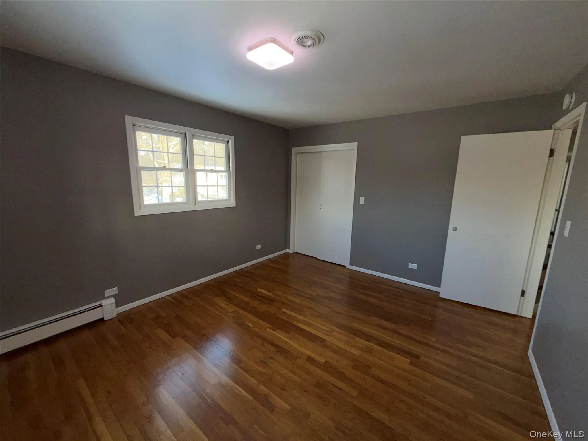 Unfurnished bedroom with a baseboard heating unit, dark wood finished floors, and a closet Unfurnished bedroom with a baseboard heating unit, dark wood finished floors, and a closet