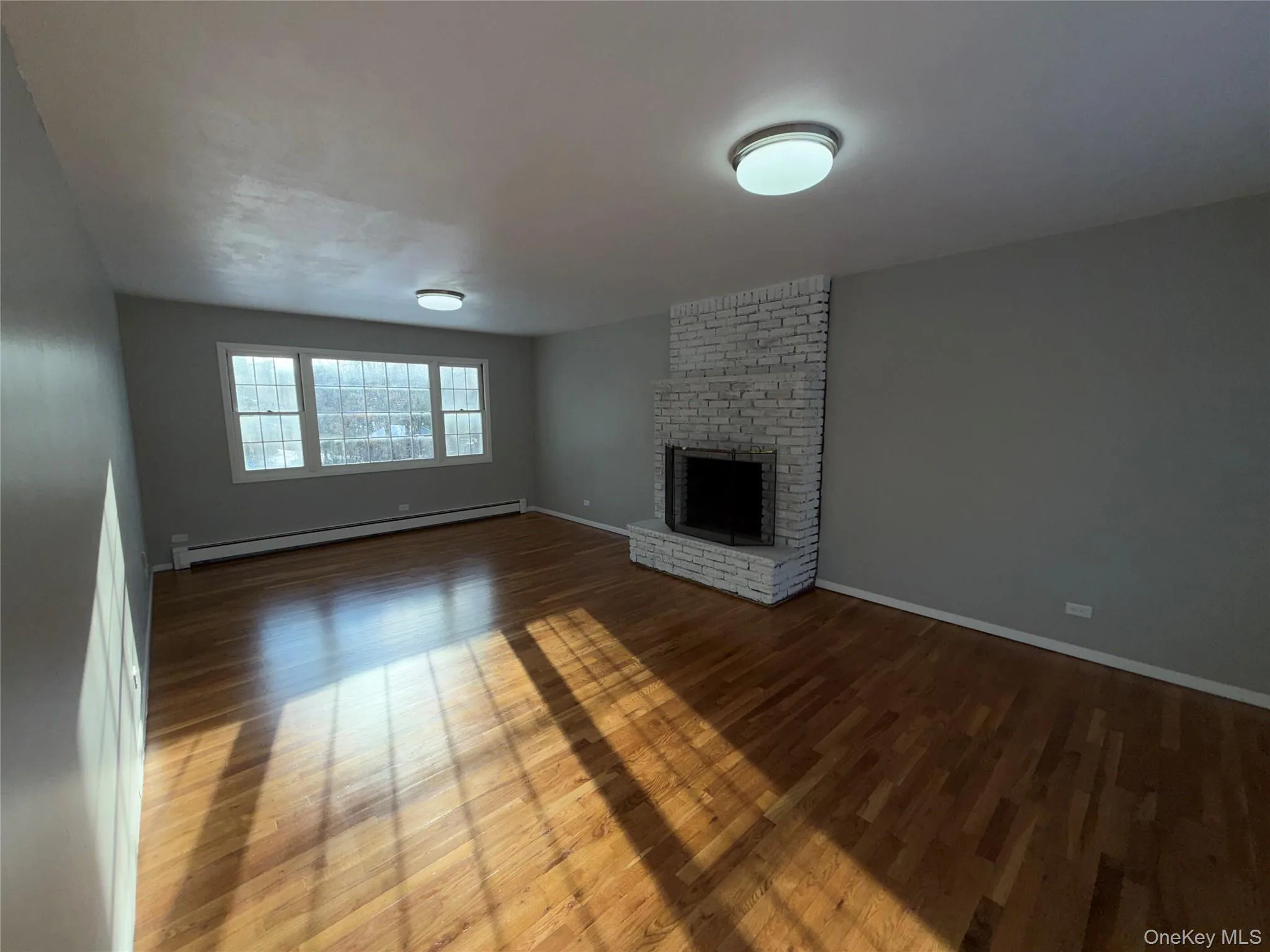 Unfurnished living room with baseboard heating, a fireplace, and wood finished floors Unfurnished living room with baseboard heating, a fireplace, and wood finished floors