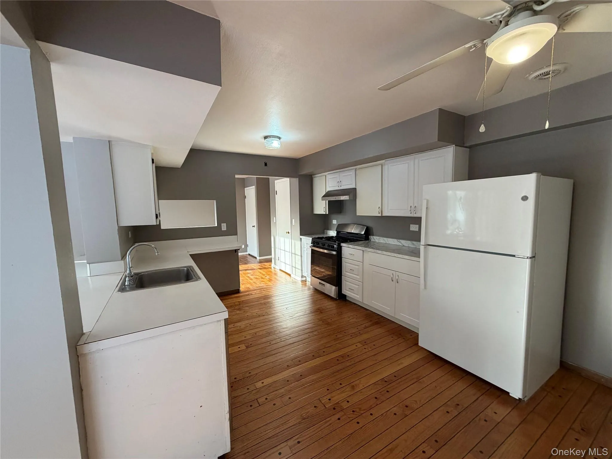 Kitchen with freestanding refrigerator, light countertops, white cabinets, and stainless steel range with gas stovetop Kitchen with freestanding refrigerator, light countertops, white cabinets, and stainless steel range with gas stovetop