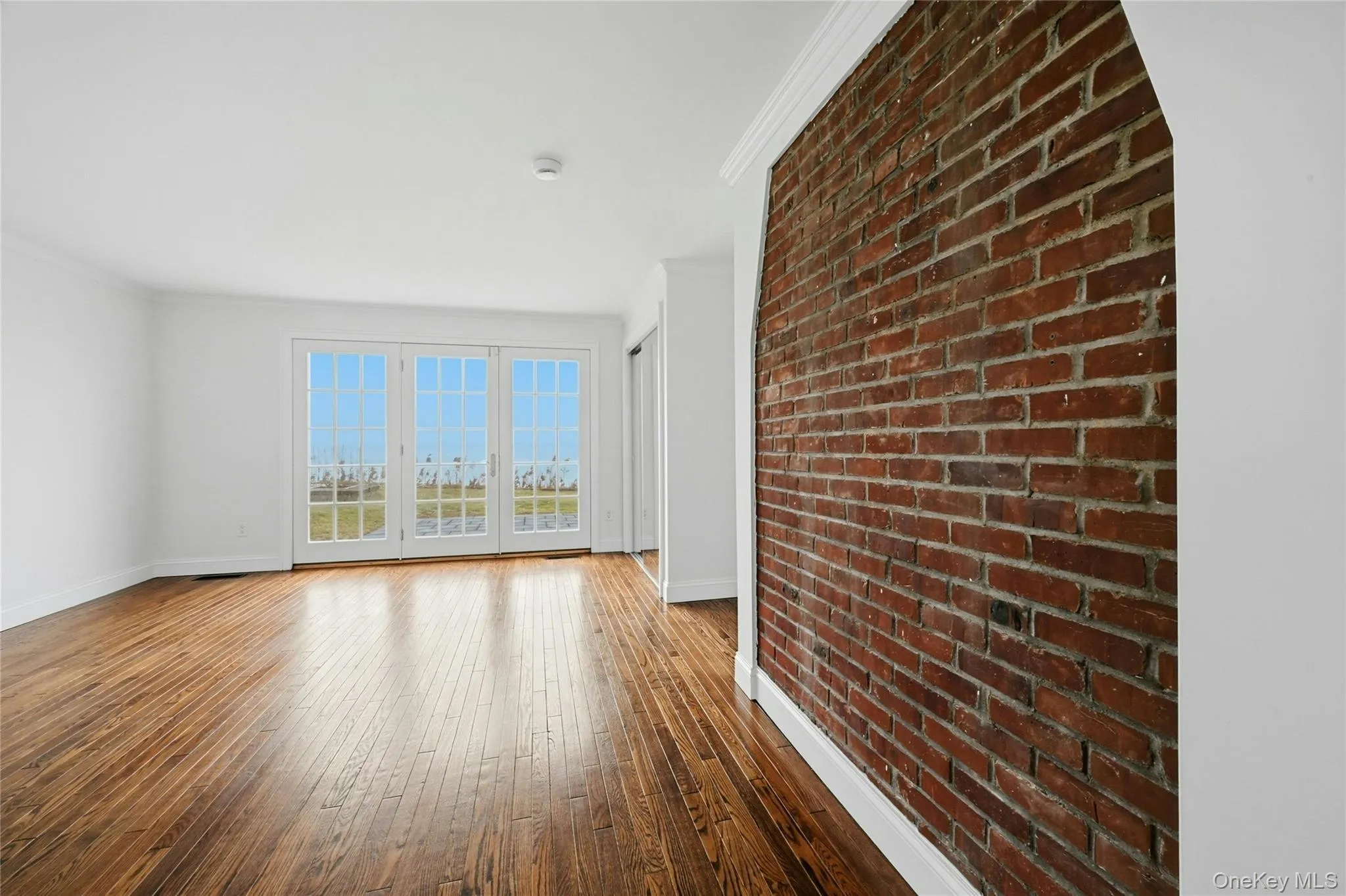 Empty room with brick wall, crown molding, and wood-type flooring Empty room with brick wall, crown molding, and wood-type flooring