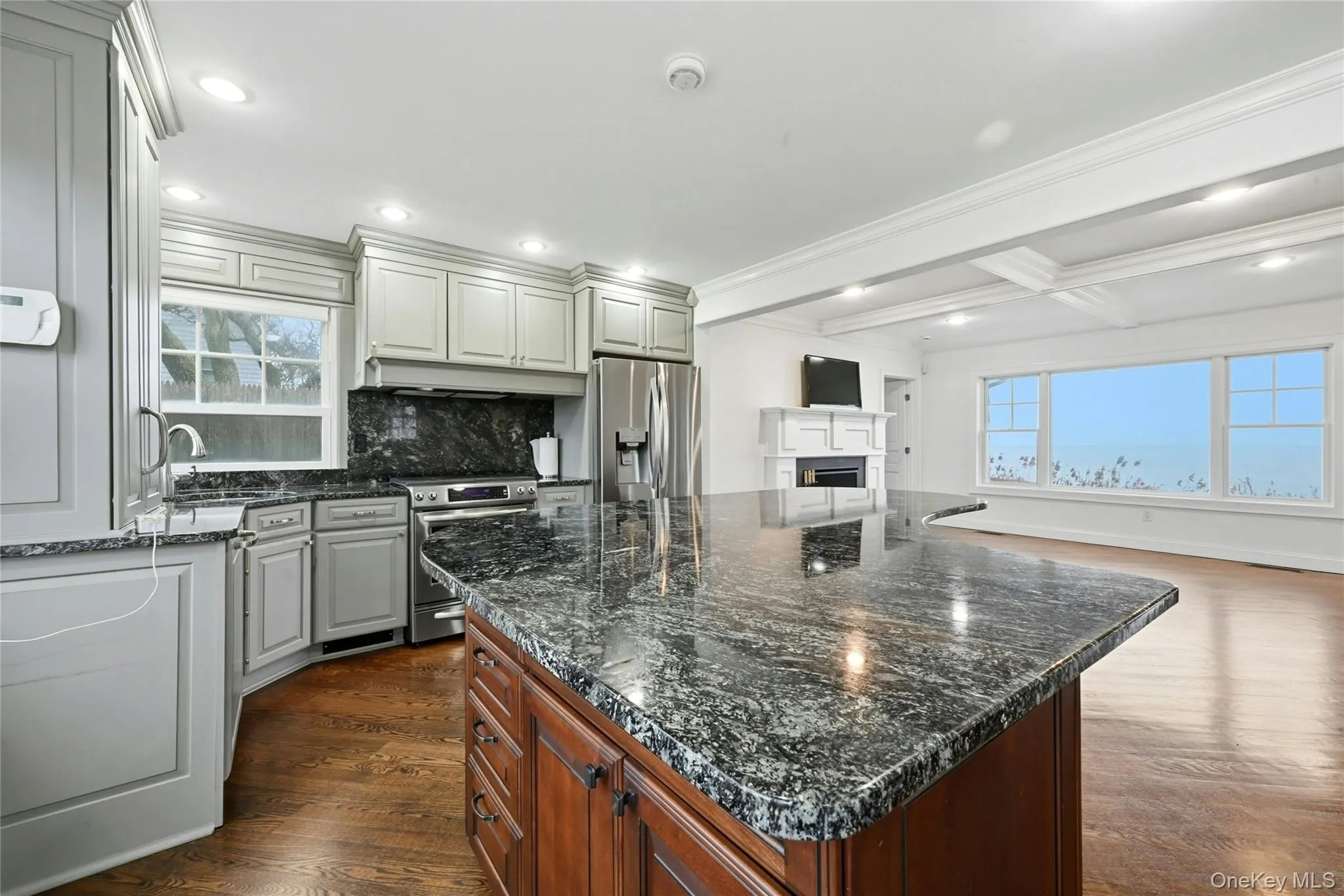 Kitchen featuring dark stone countertops, dark wood-style floors, crown molding, appliances with stainless steel finishes, and backsplash Kitchen featuring dark stone countertops, dark wood-style floors, crown molding, appliances with stainless steel finishes, and backsplash