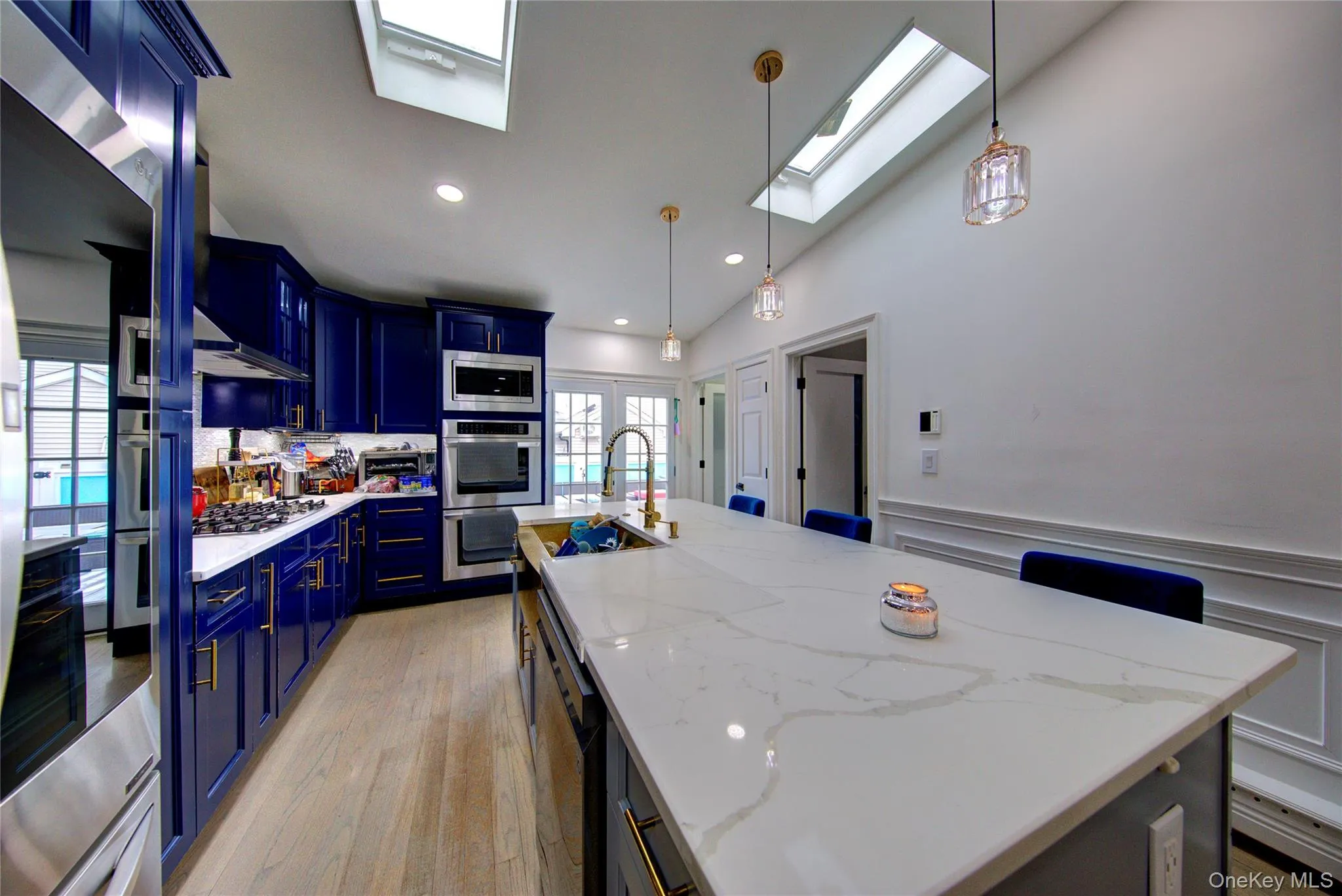 Kitchen featuring a center island with sink, stainless steel appliances, blue cabinets, pendant lighting, and light stone countertops Kitchen featuring a center island with sink, stainless steel appliances, blue cabinets, pendant lighting, and light stone countertops