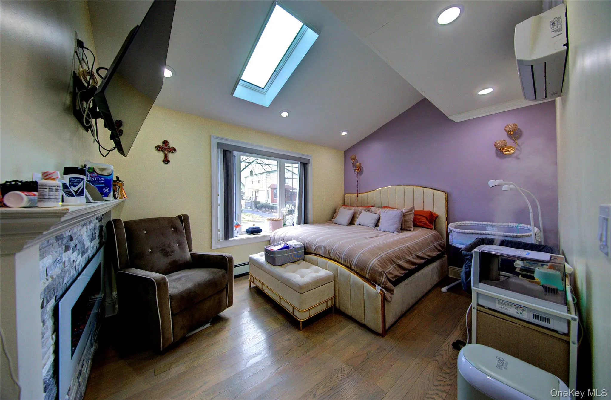Bedroom with vaulted ceiling, a wall unit AC, a skylight, a stone fireplace, and hardwood / wood-style flooring Bedroom with vaulted ceiling, a wall unit AC, a skylight, a stone fireplace, and hardwood / wood-style flooring