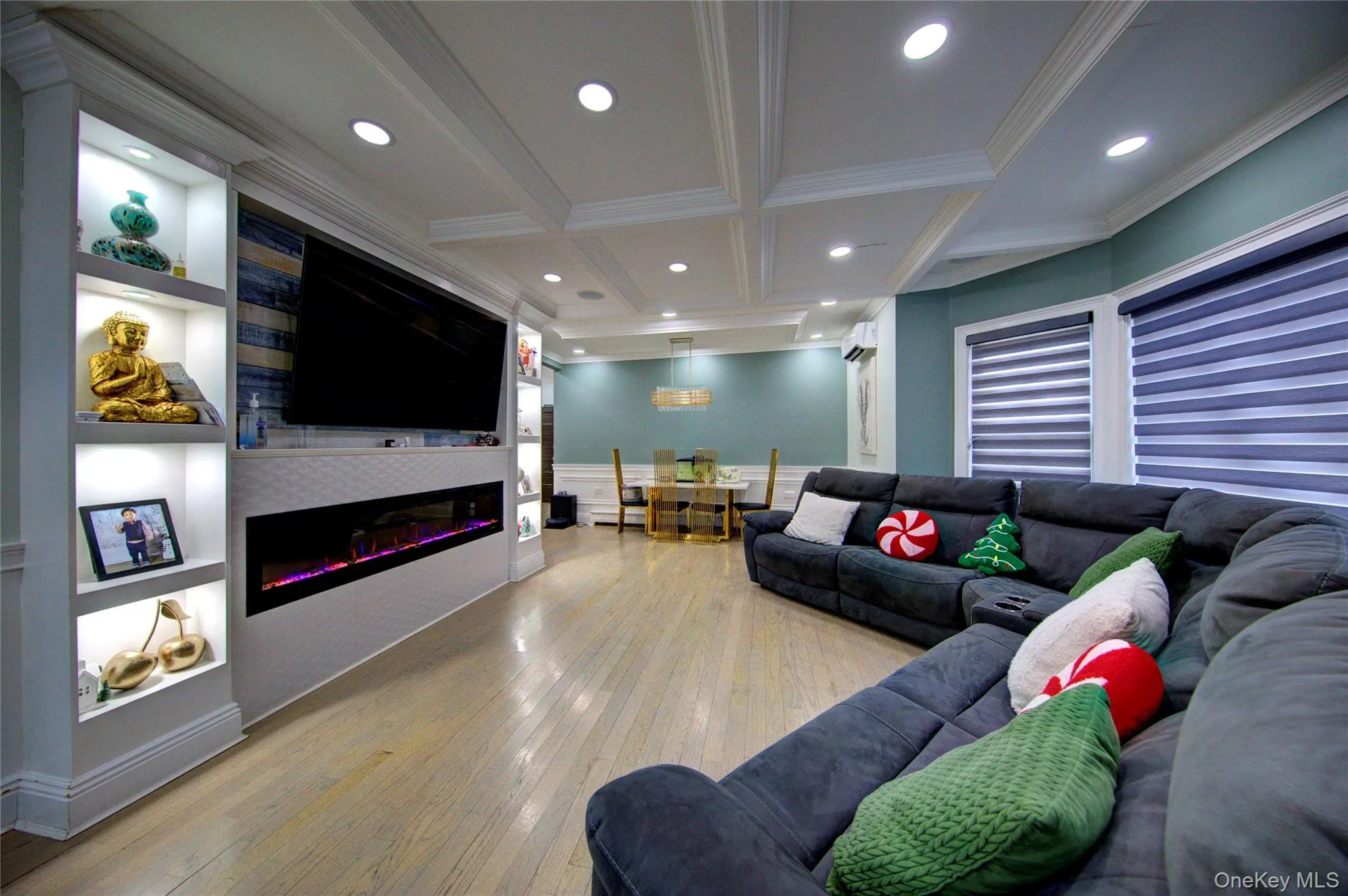 Living area with built in shelves, a glass covered fireplace, beam ceiling, wood-type flooring, and coffered ceiling Living area with built in shelves, a glass covered fireplace, beam ceiling, wood-type flooring, and coffered ceiling