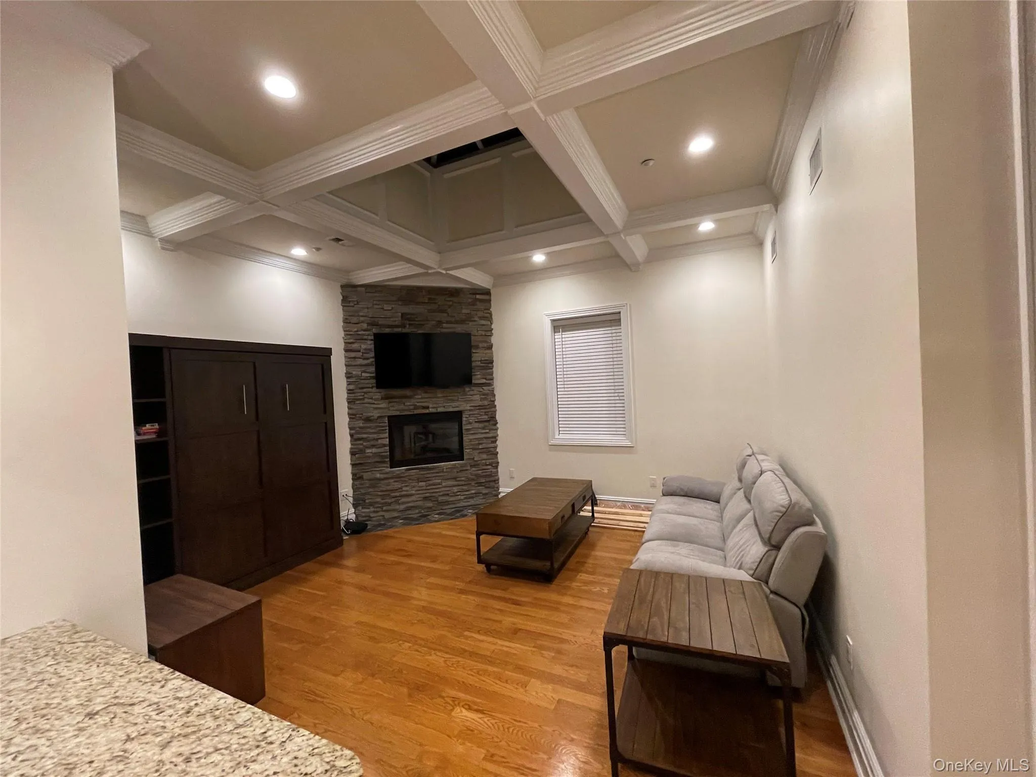 Living room with coffered ceiling, light wood-style floors, beamed ceiling, a stone fireplace, and recessed lighting Living room with coffered ceiling, light wood-style floors, beamed ceiling, a stone fireplace, and recessed lighting