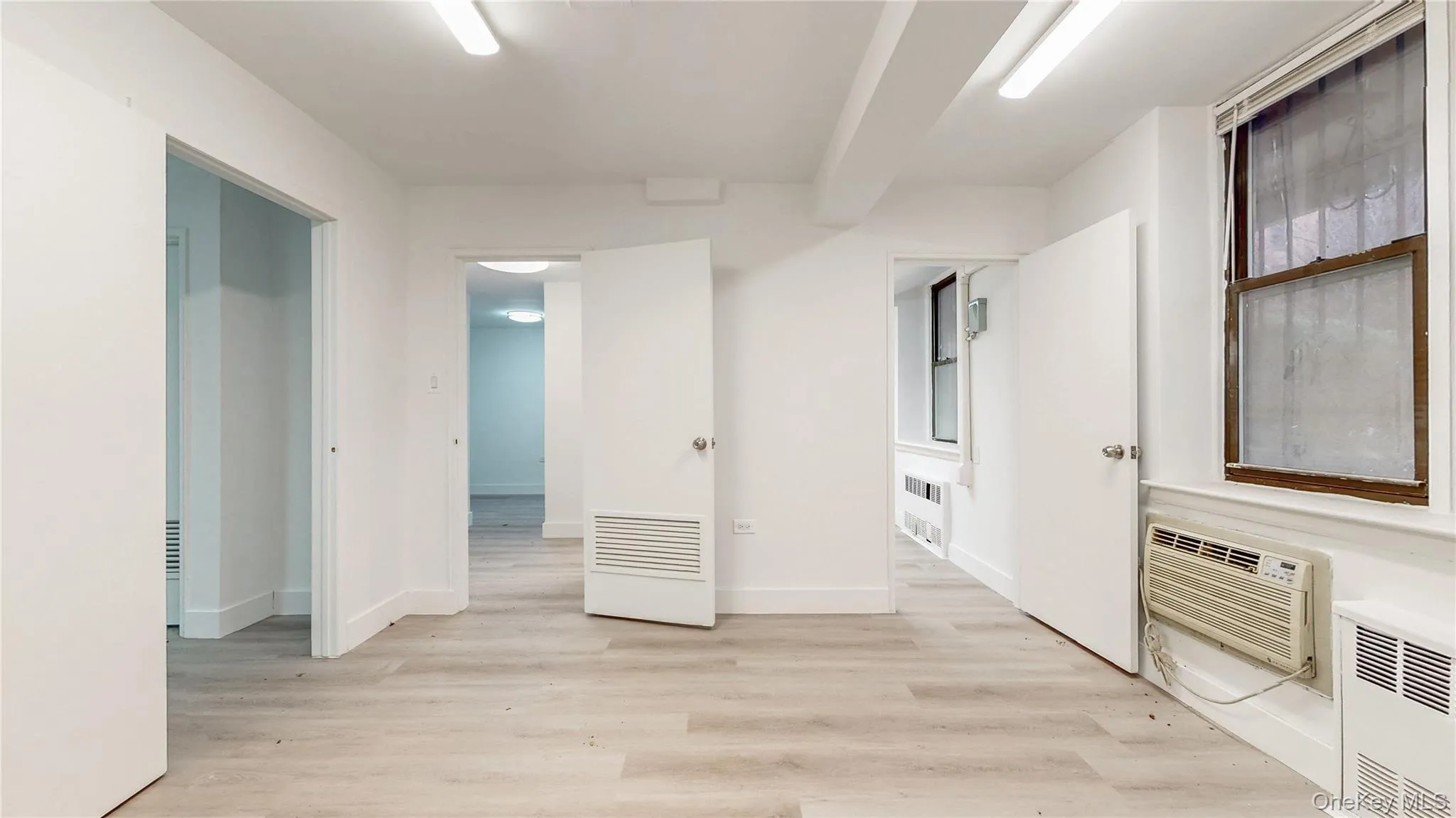 Spare room with light wood-style floors, a wall unit AC, and radiator Spare room with light wood-style floors, a wall unit AC, and radiator