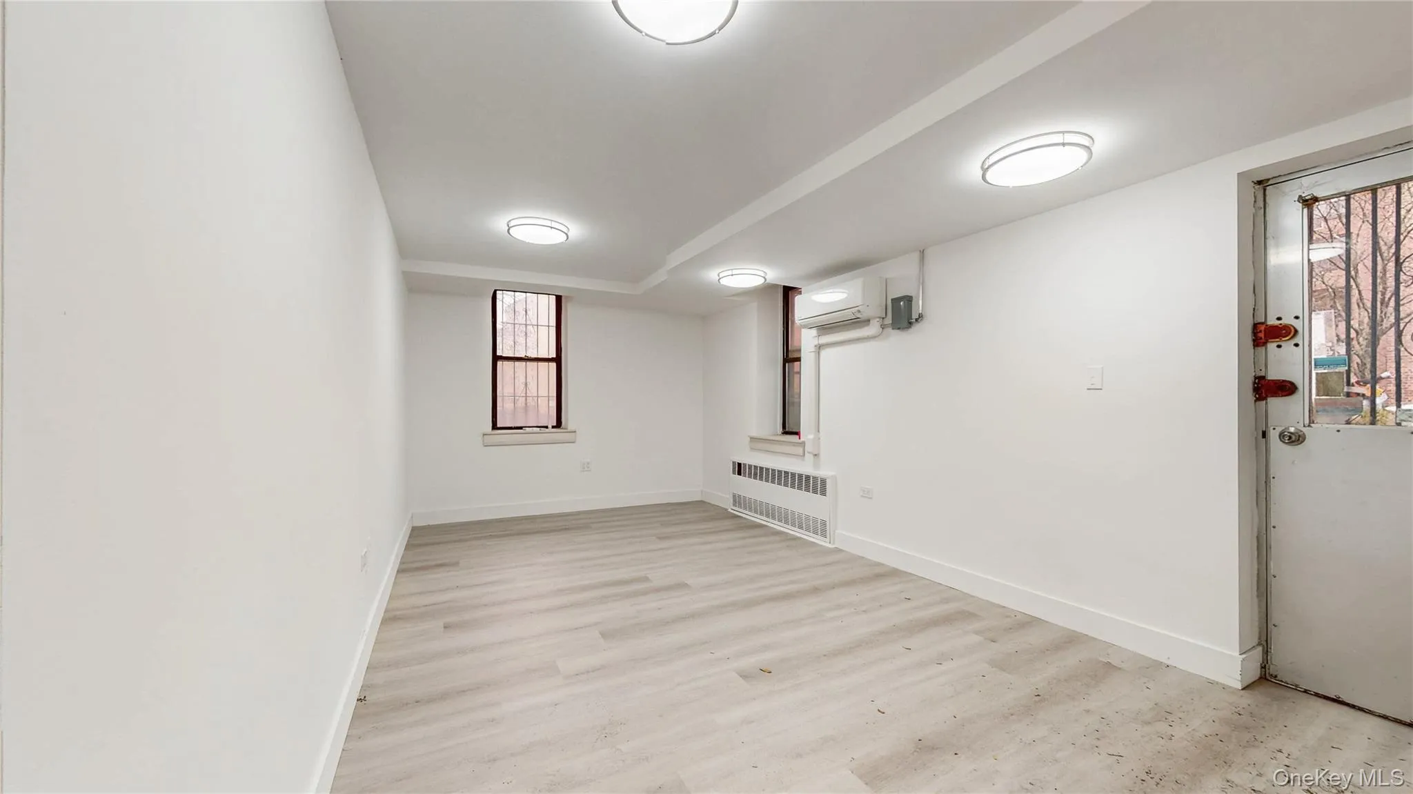 Basement with light wood-type flooring, radiator, and a wall unit AC Basement with light wood-type flooring, radiator, and a wall unit AC