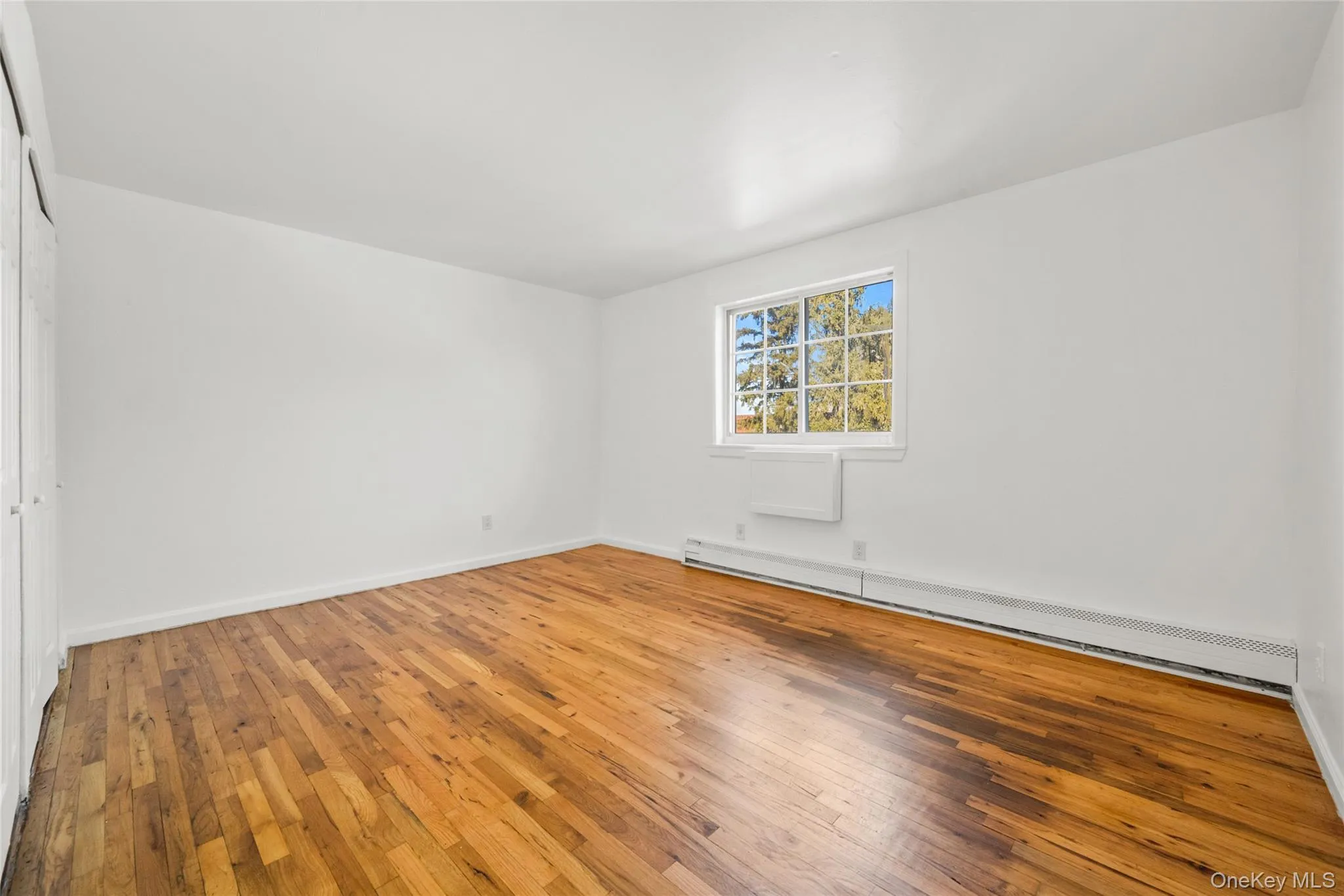 Unfurnished room featuring baseboard heating and wood-type flooring Unfurnished room featuring baseboard heating and wood-type flooring