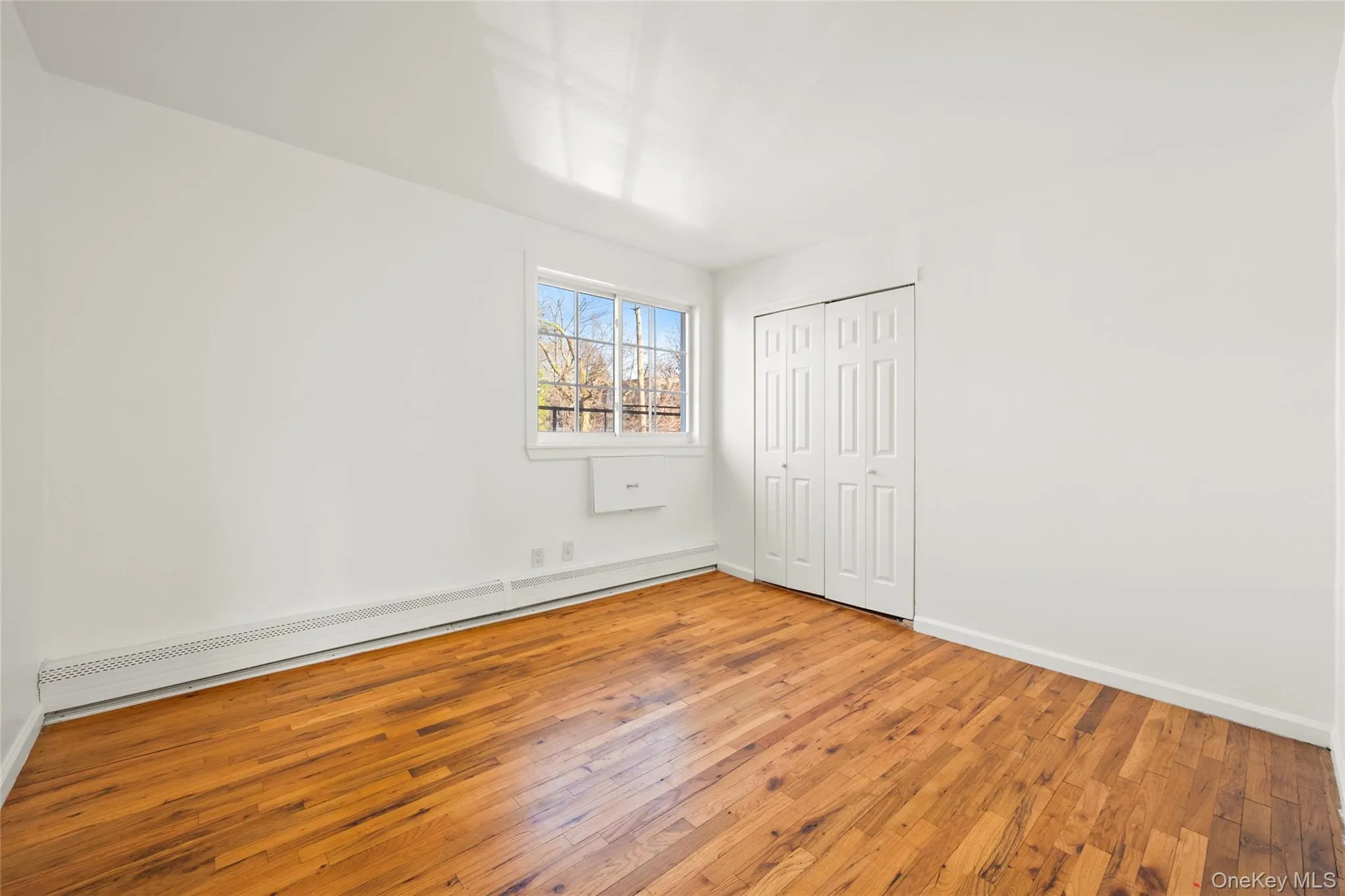Unfurnished bedroom with a baseboard heating unit, hardwood / wood-style flooring, and a closet Unfurnished bedroom with a baseboard heating unit, hardwood / wood-style flooring, and a closet