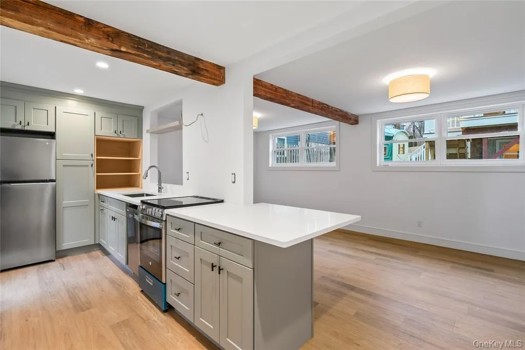 Kitchen with gray cabinets, stainless steel appliances, light wood-style flooring, a peninsula, and beam ceiling Kitchen with gray cabinets, stainless steel appliances, light wood-style flooring, a peninsula, and beam ceiling