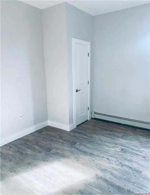 Unfurnished room featuring a baseboard radiator and dark wood-style flooring Unfurnished room featuring a baseboard radiator and dark wood-style flooring