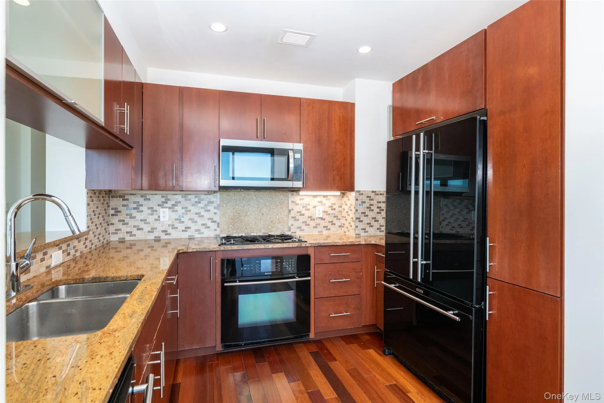 Kitchen with light stone countertops, black appliances, dark wood-type flooring, tasteful backsplash, and recessed lighting Kitchen with light stone countertops, black appliances, dark wood-type flooring, tasteful backsplash, and recessed lighting