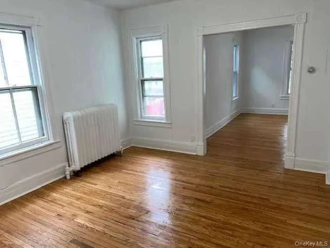 Unfurnished room featuring radiator heating unit and light wood-style flooring Unfurnished room featuring radiator heating unit and light wood-style flooring