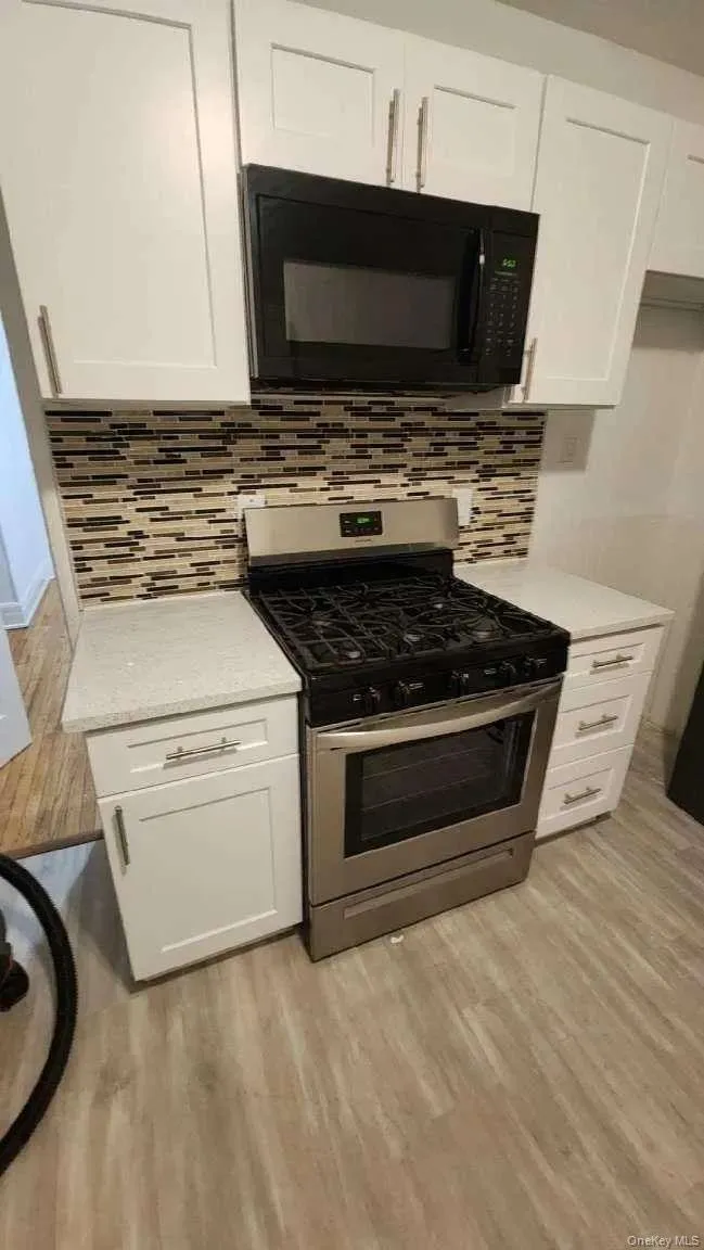 Kitchen featuring stainless steel range with gas cooktop, black microwave, white cabinets, and light wood-style flooring Kitchen featuring stainless steel range with gas cooktop, black microwave, white cabinets, and light wood-style flooring