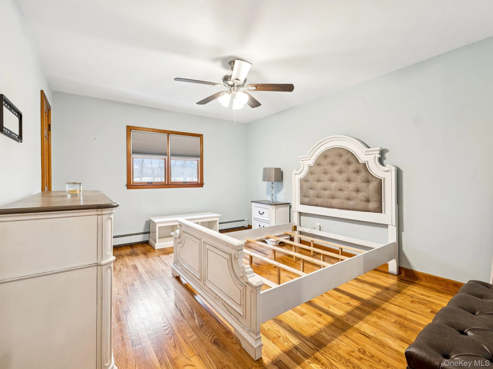 Bedroom with light wood finished floors, ceiling fan, and a baseboard heating unit Bedroom with light wood finished floors, ceiling fan, and a baseboard heating unit