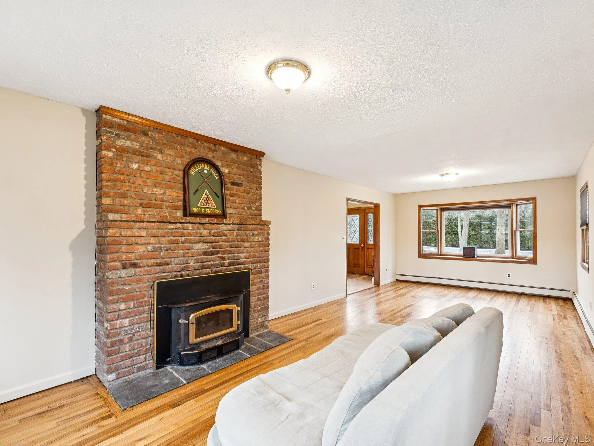 Living room featuring light wood-style floors, a textured ceiling, baseboard heating, and a fireplace Living room featuring light wood-style floors, a textured ceiling, baseboard heating, and a fireplace