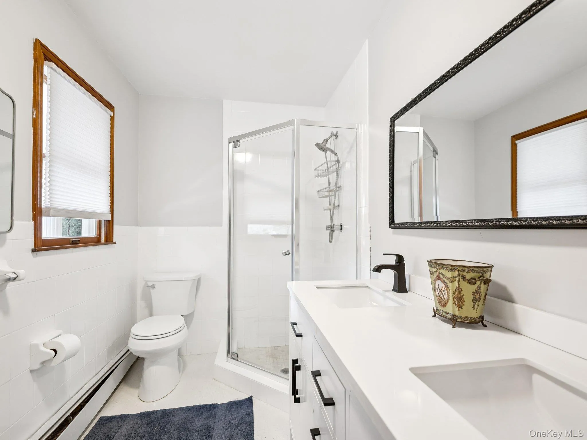 Bathroom featuring double vanity, baseboard heating, a stall shower, a wainscoted wall, and light tile patterned flooring Bathroom featuring double vanity, baseboard heating, a stall shower, a wainscoted wall, and light tile patterned flooring