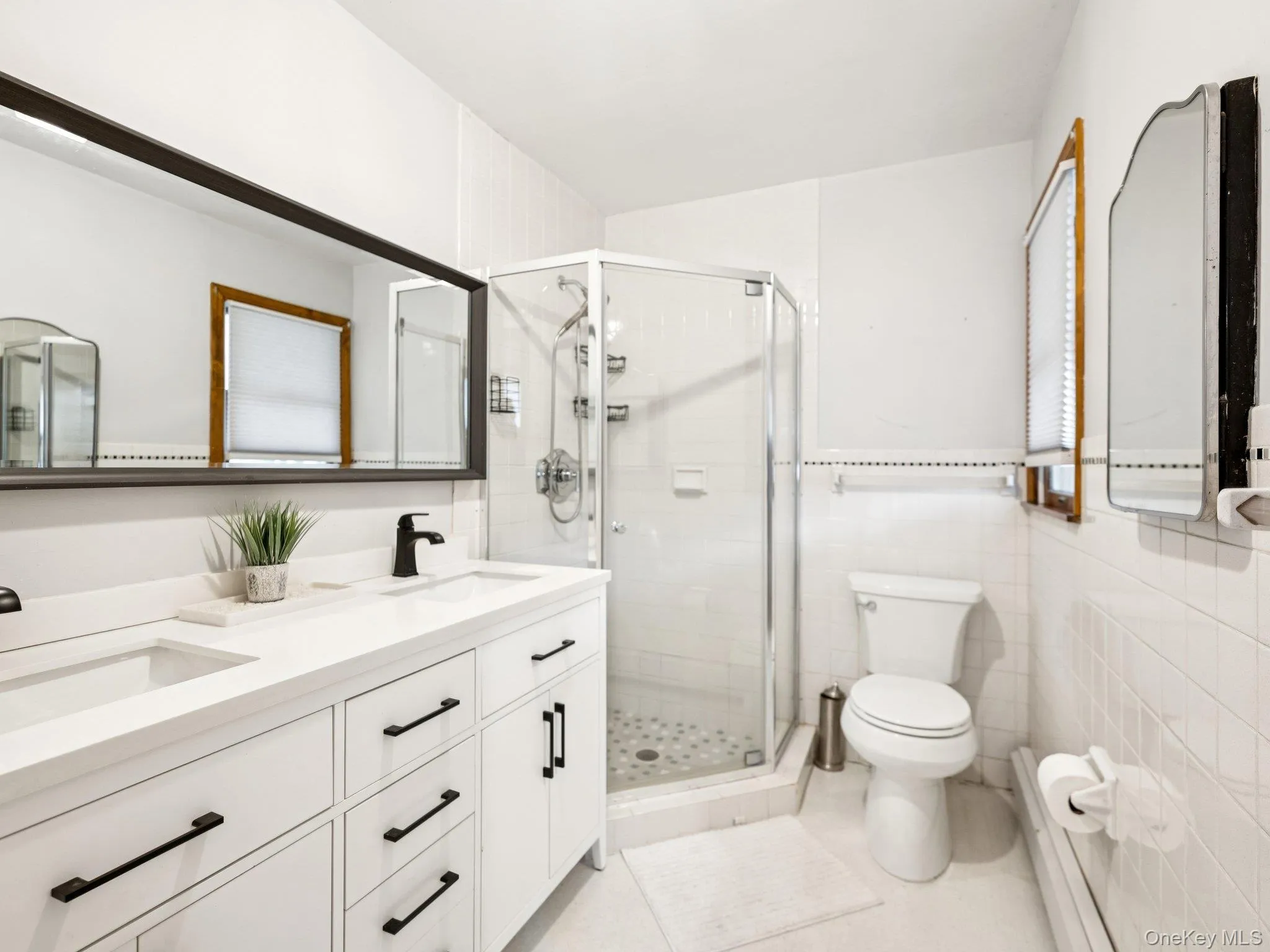 Full bathroom with double vanity, a shower stall, light tile patterned floors, a baseboard radiator, and tile walls Full bathroom with double vanity, a shower stall, light tile patterned floors, a baseboard radiator, and tile walls