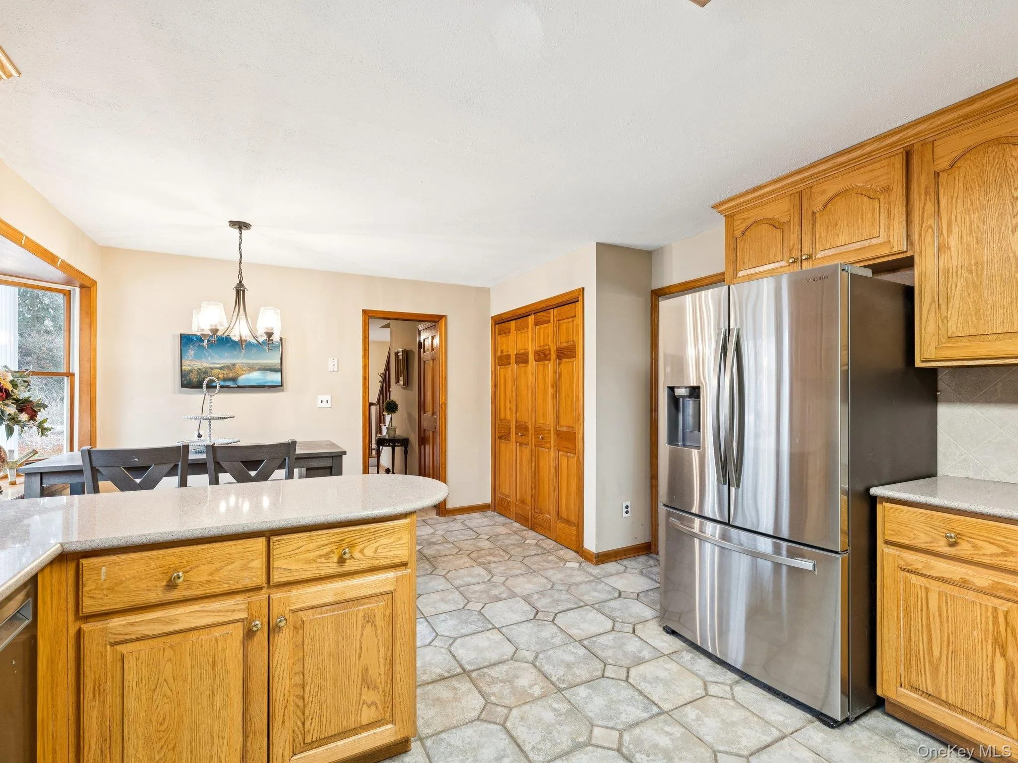 Kitchen with appliances with stainless steel finishes, hanging light fixtures, a chandelier, brown cabinetry, and light stone counters Kitchen with appliances with stainless steel finishes, hanging light fixtures, a chandelier, brown cabinetry, and light stone counters