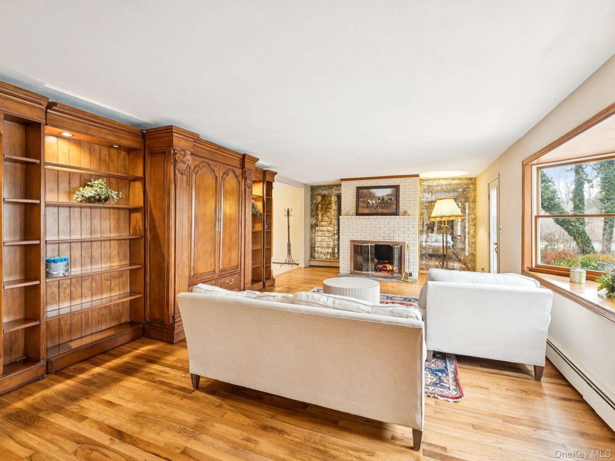 Living room featuring a brick fireplace, baseboard heating, light wood-style floors, and built in features Living room featuring a brick fireplace, baseboard heating, light wood-style floors, and built in features