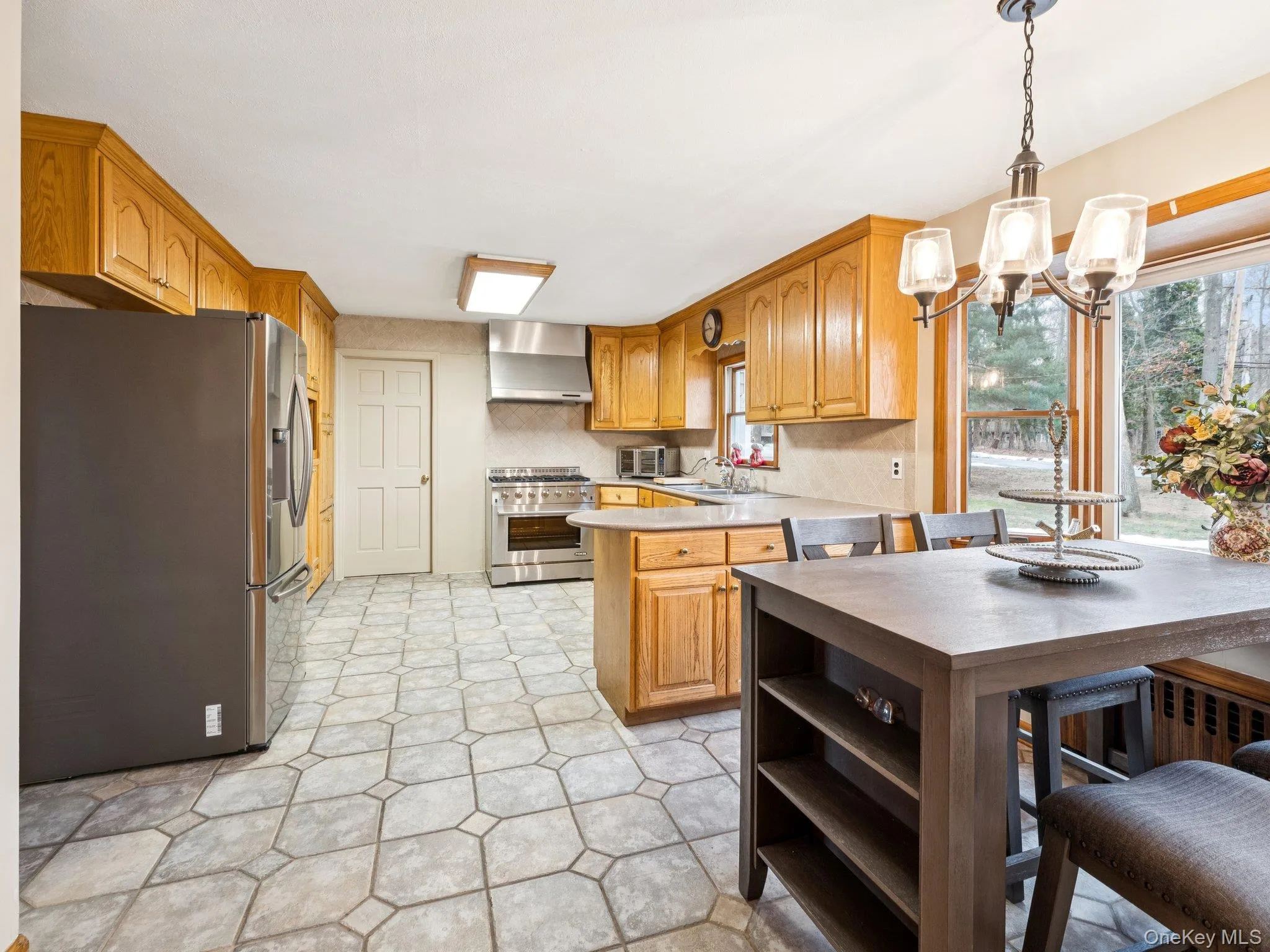 Kitchen featuring appliances with stainless steel finishes, a peninsula, light countertops, pendant lighting, and wall chimney range hood Kitchen featuring appliances with stainless steel finishes, a peninsula, light countertops, pendant lighting, and wall chimney range hood