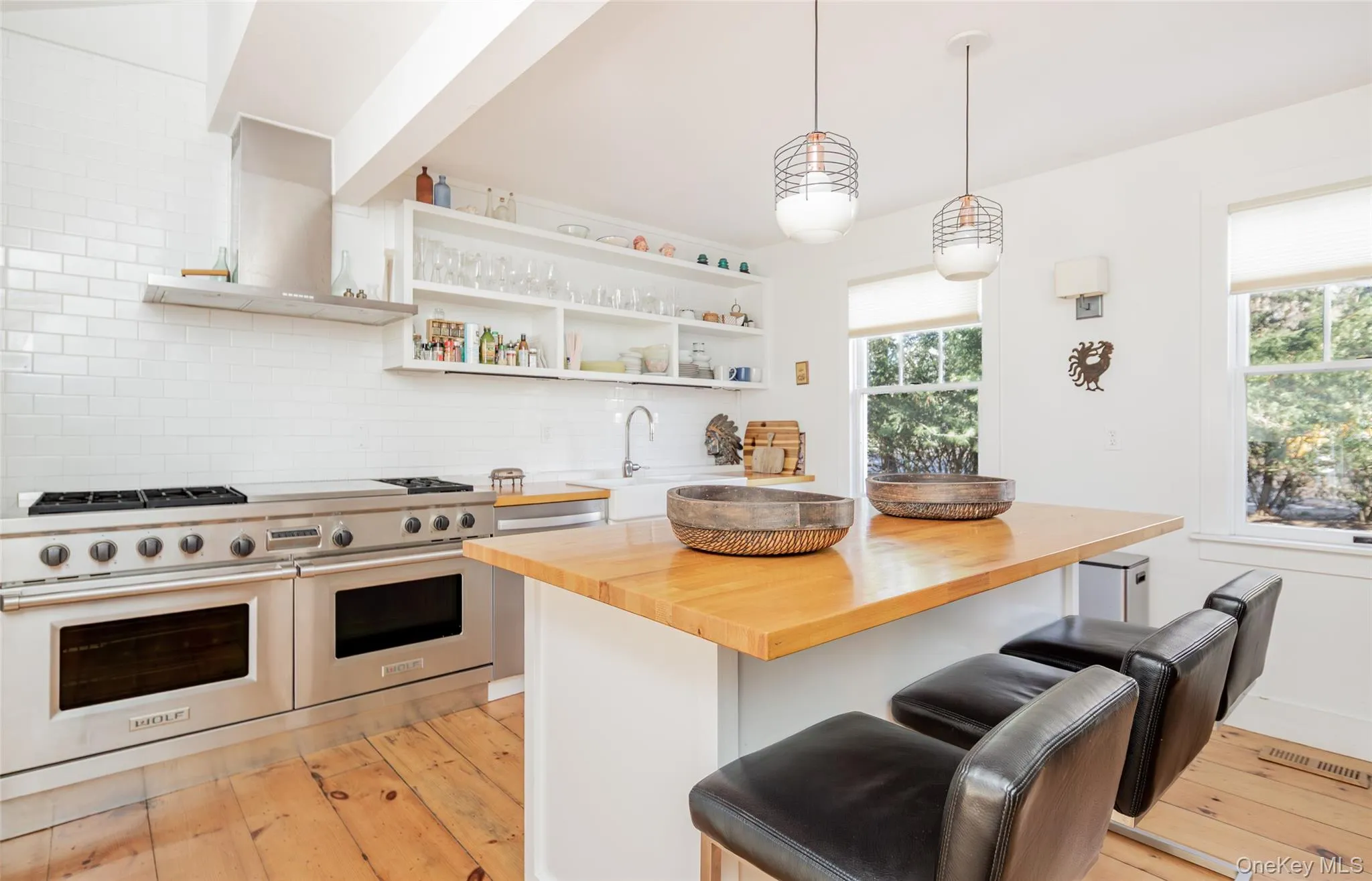 Kitchen featuring butcher block countertops, pendant lighting, range with two ovens, wall chimney exhaust hood, and tasteful backsplash Kitchen featuring butcher block countertops, pendant lighting, range with two ovens, wall chimney exhaust hood, and tasteful backsplash