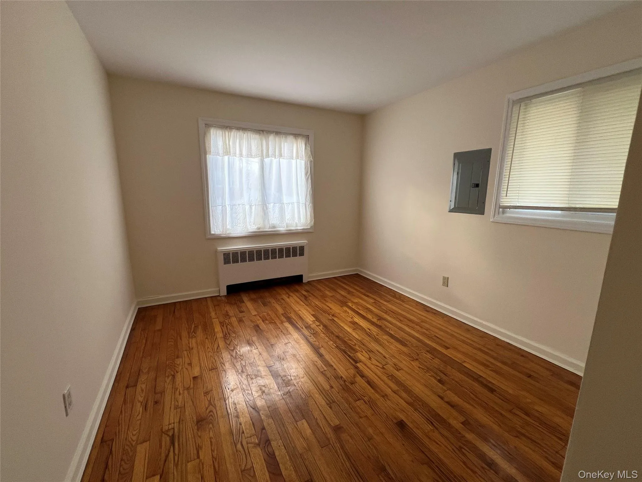 Unfurnished room with wood-type flooring, electric panel, and radiator Unfurnished room with wood-type flooring, electric panel, and radiator