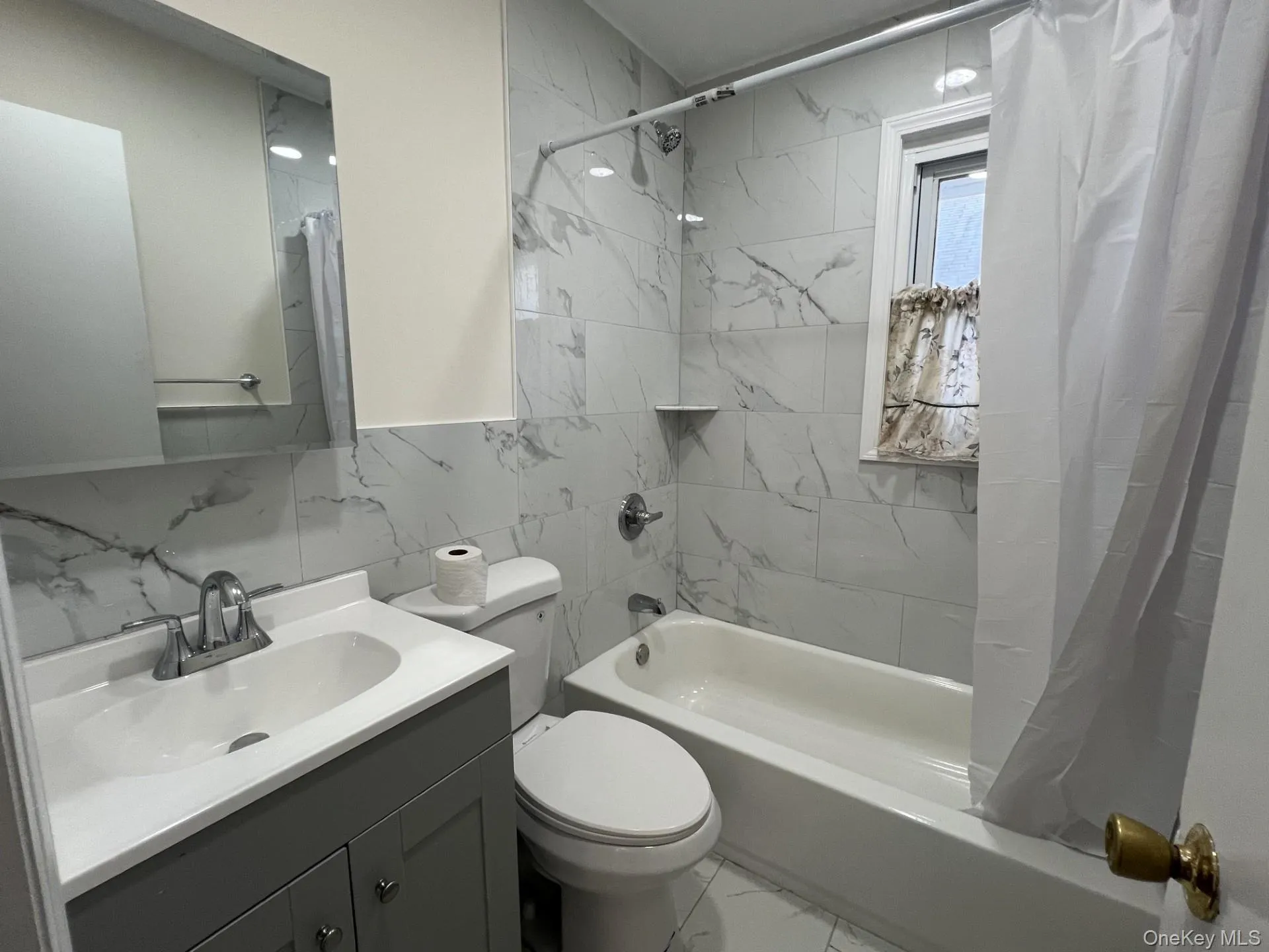 Bathroom featuring tile walls, shower / bath combo with shower curtain, vanity, and light marble finish floors Bathroom featuring tile walls, shower / bath combo with shower curtain, vanity, and light marble finish floors
