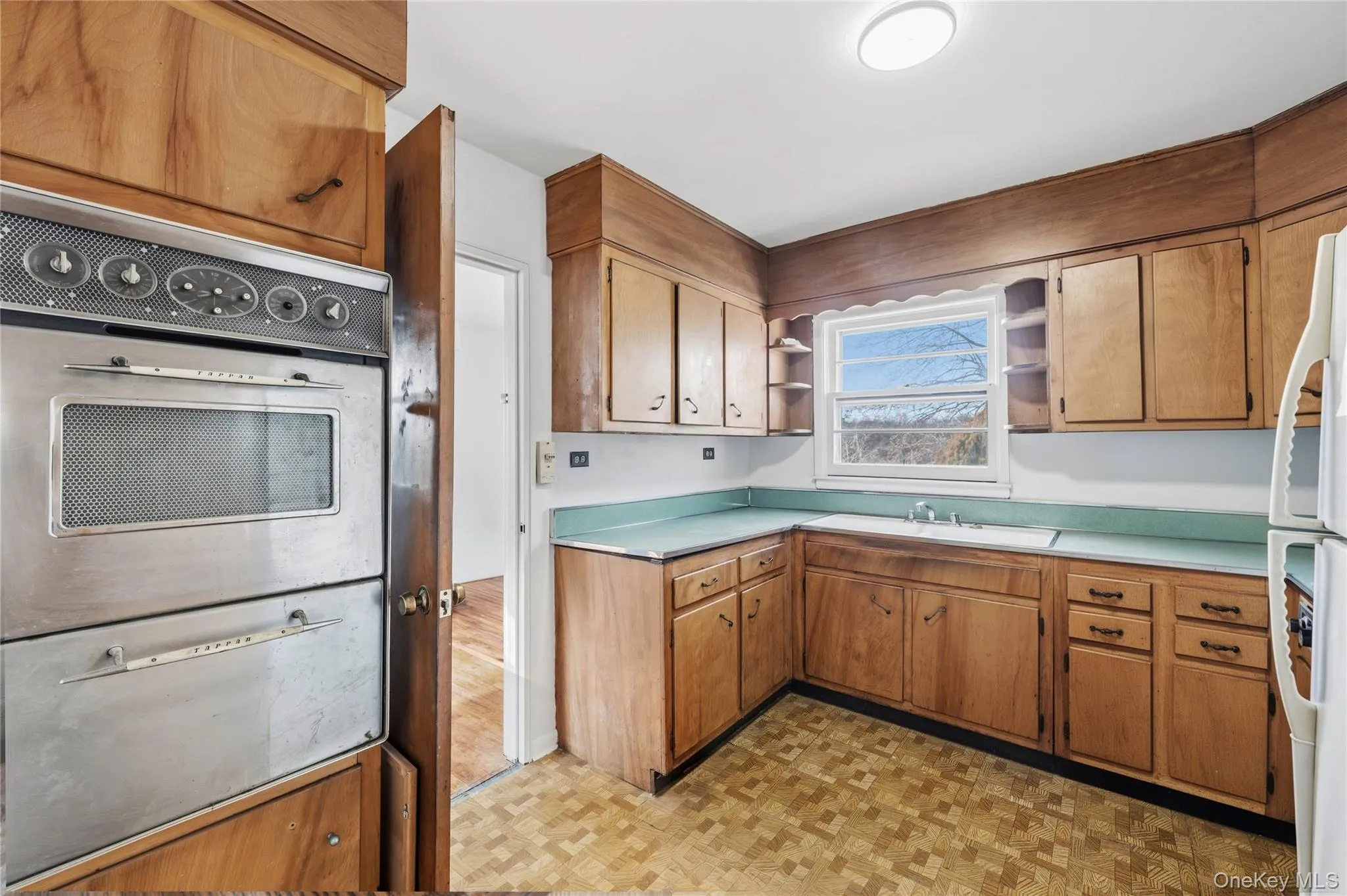 Kitchen with open shelves, a warming drawer, light countertops, stainless steel oven, and brown cabinets Kitchen with open shelves, a warming drawer, light countertops, stainless steel oven, and brown cabinets