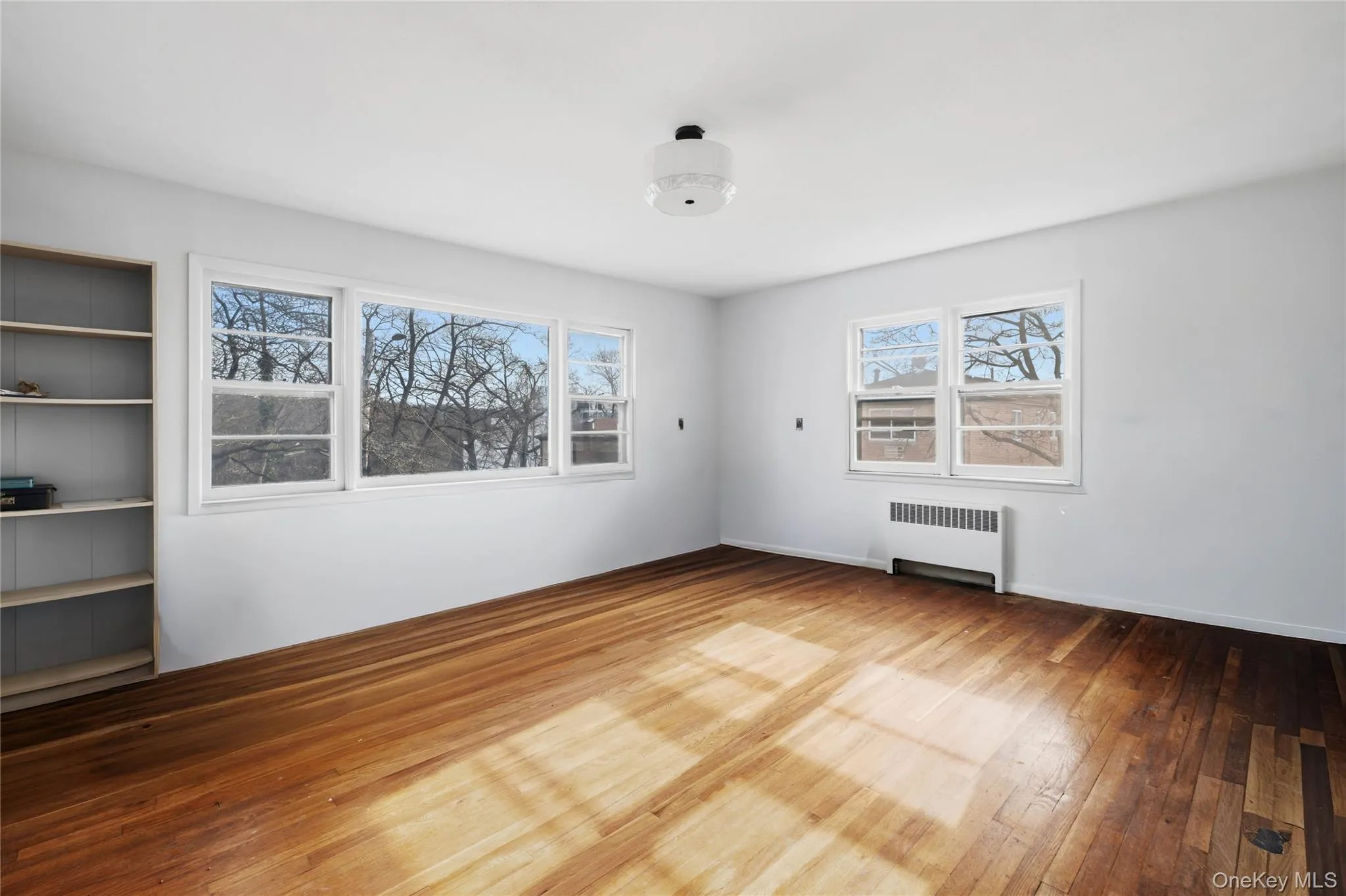 Unfurnished room featuring radiator and hardwood / wood-style flooring Unfurnished room featuring radiator and hardwood / wood-style flooring